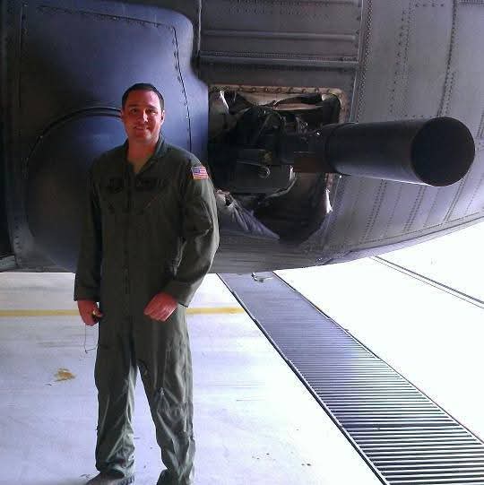 Person in military jumpsuit standing next to aircraft engine inside hangar.