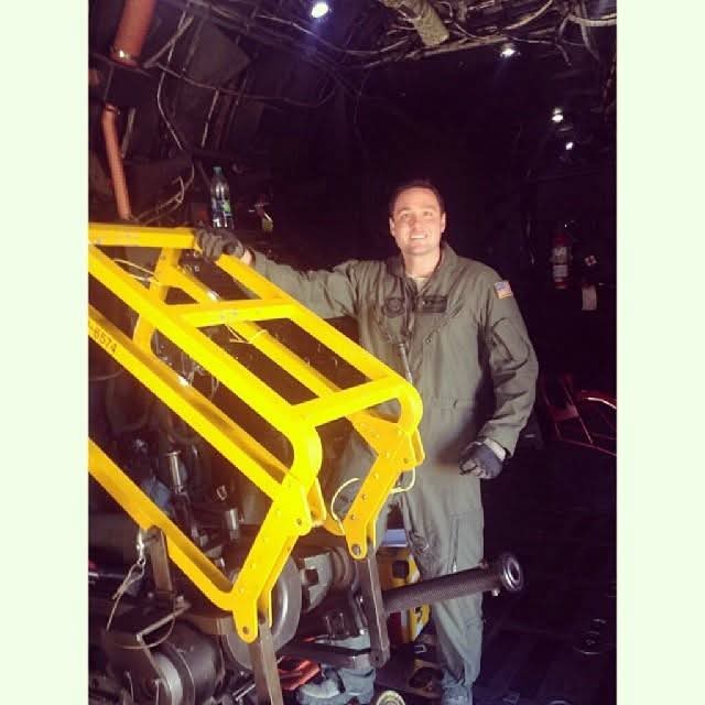 Person in a gray jumpsuit standing next to a yellow mechanical structure in a dark environment.