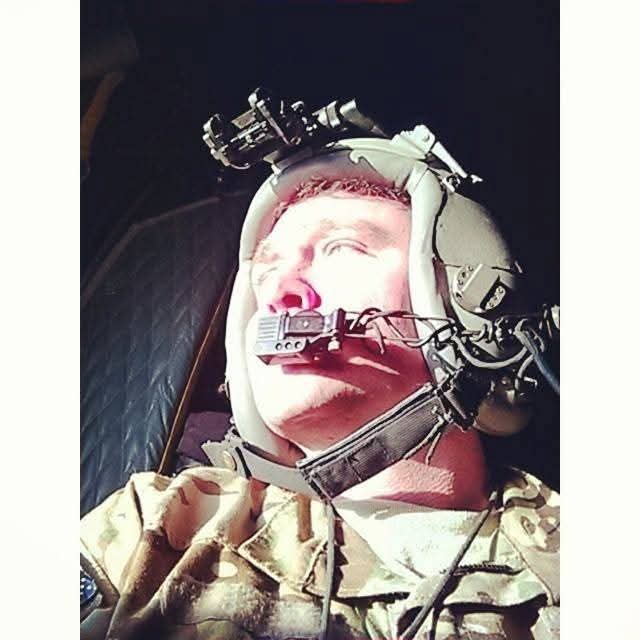 Person in a helmet with equipment, lying down with eyes closed, illuminated by bright light, wearing camouflage clothing.