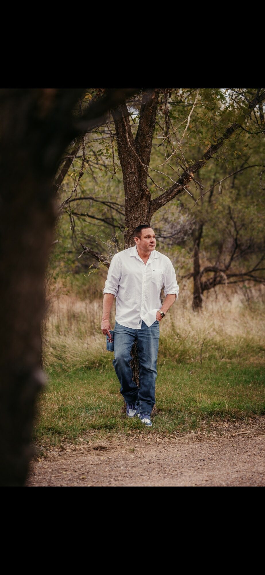 Man walking outdoors in a grassy area with trees in the background.