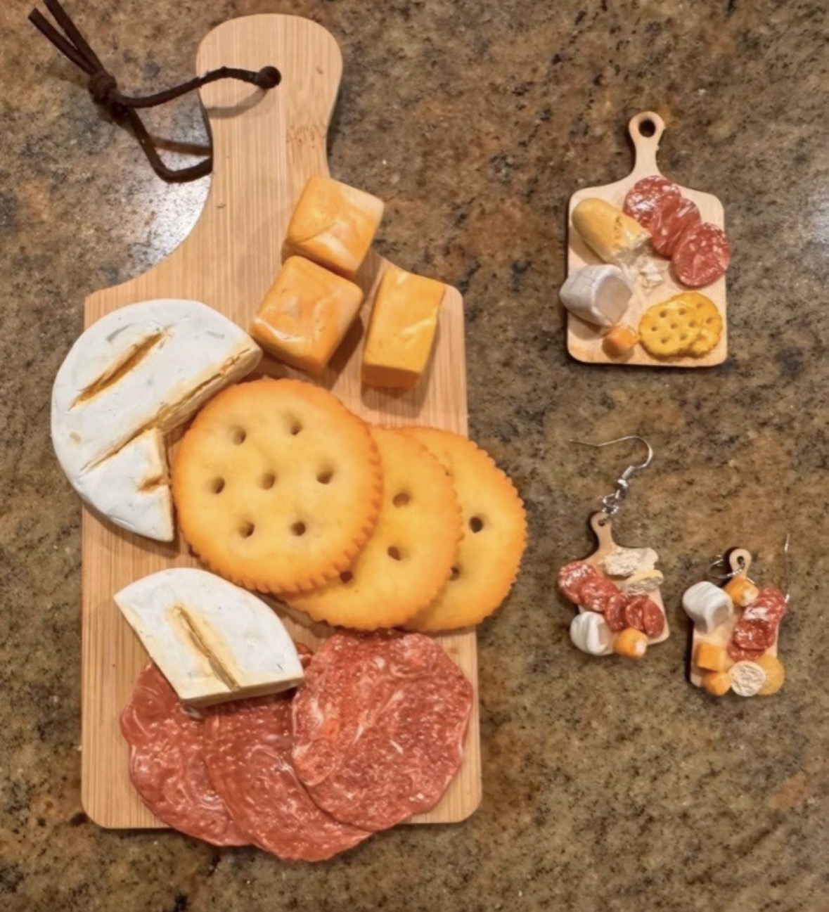 Cheese, crackers, sliced bread, salami, and small charcuterie items on a wooden board on a brown surface.