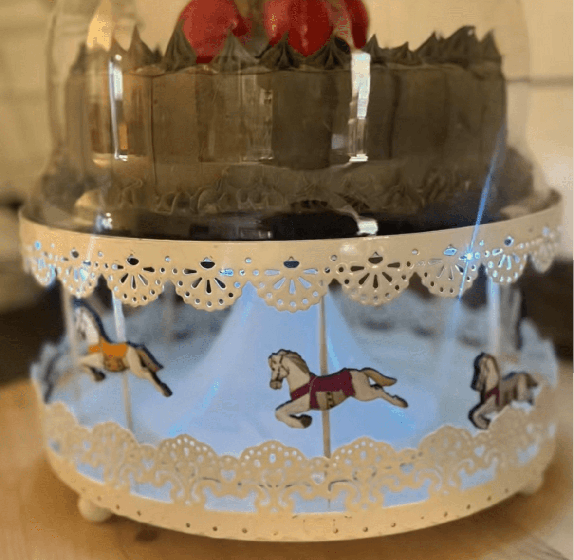 Decorative carousel with three horses, lace-like trim, and a glass dome on top, containing red flowers inside.