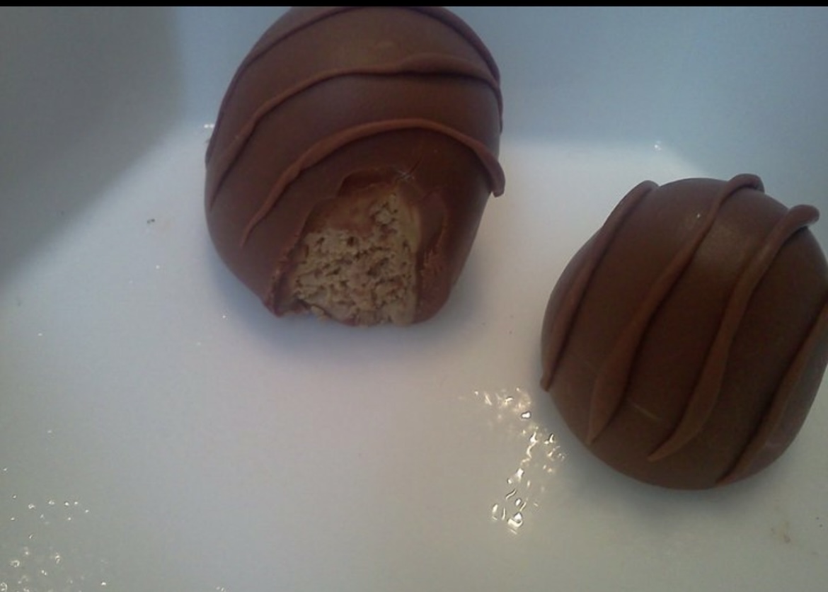 Two round chocolate-covered confections, one partially bitten, on a white surface.