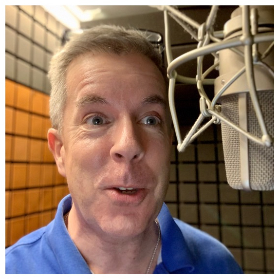 Man in blue shirt speaking into a microphone in recording studio with soundproof walls.