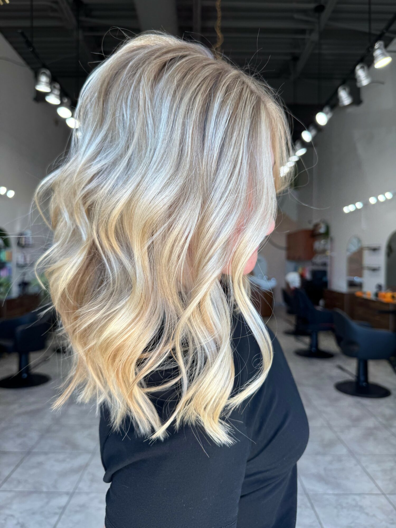 Side view of a woman with wavy, blonde hair in a salon setting.