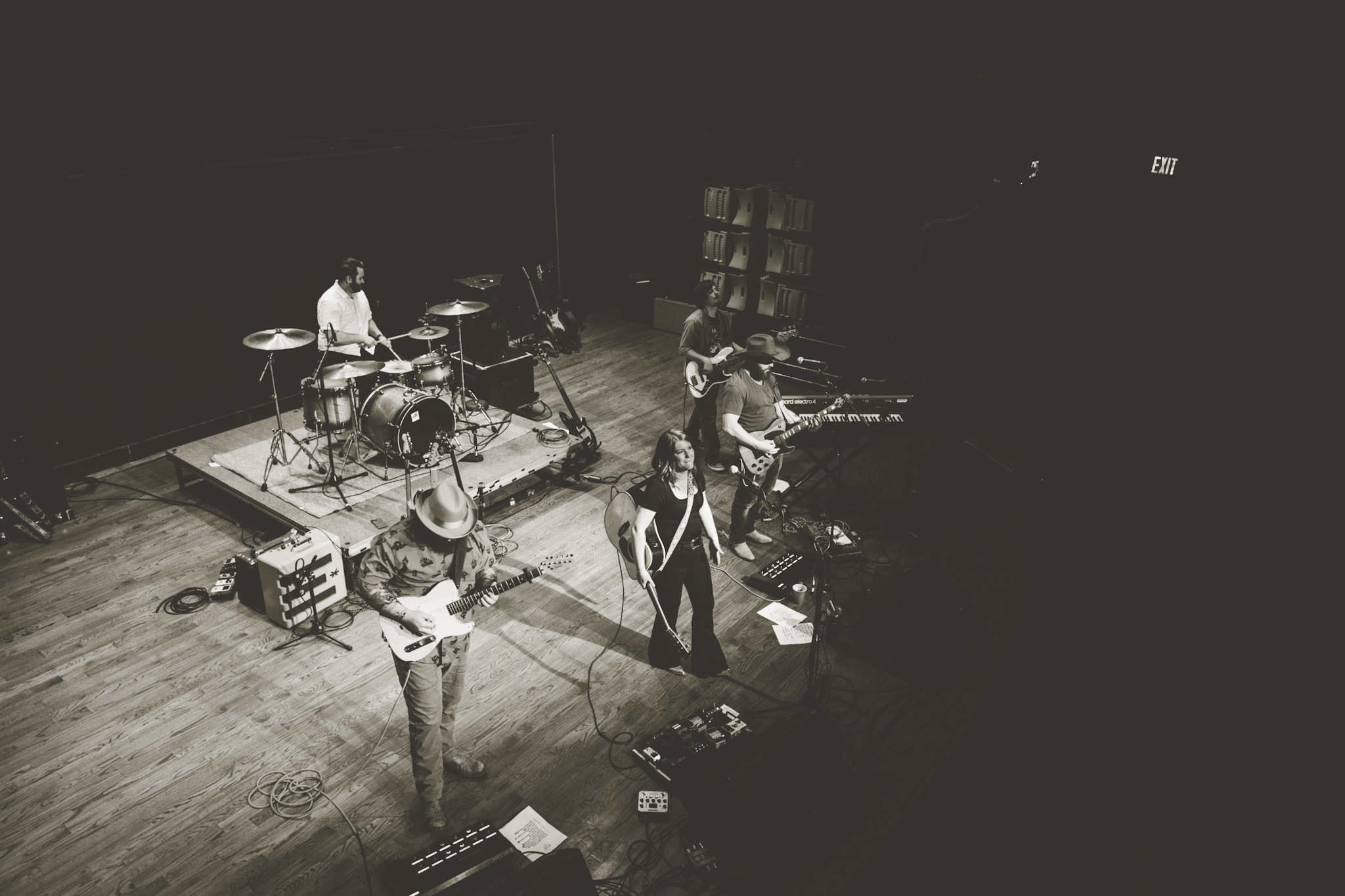 Band performs on stage with five musicians, instruments, and equipment in a dark setting.