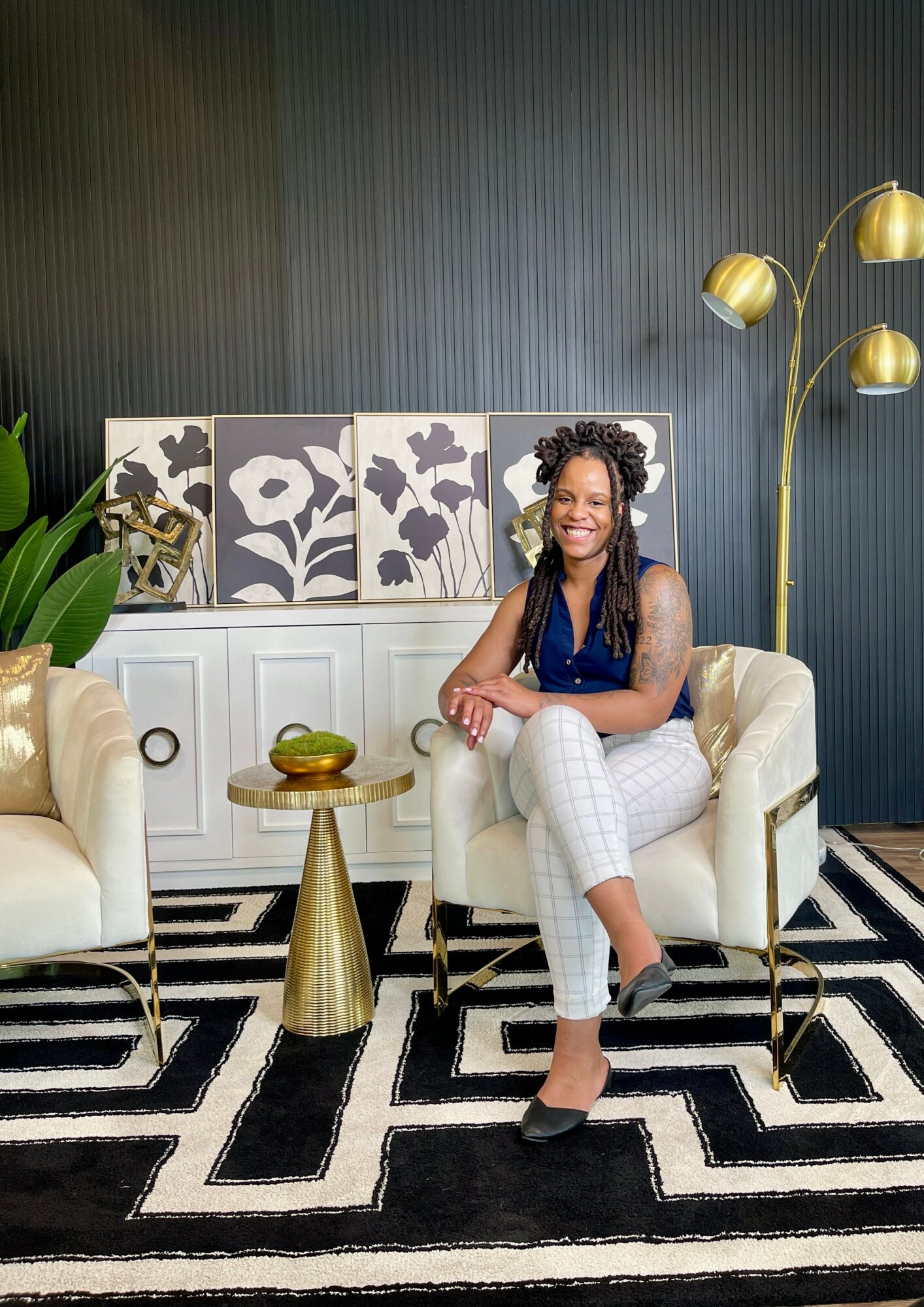 Woman sitting on a white sofa in a modern room with black and white geometric rug, gold floor lamp, and decorative art.