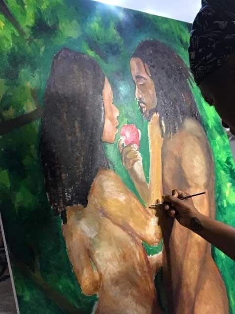 Two women with long dark hair face each other, one holding a pink flower, in a green outdoor setting.