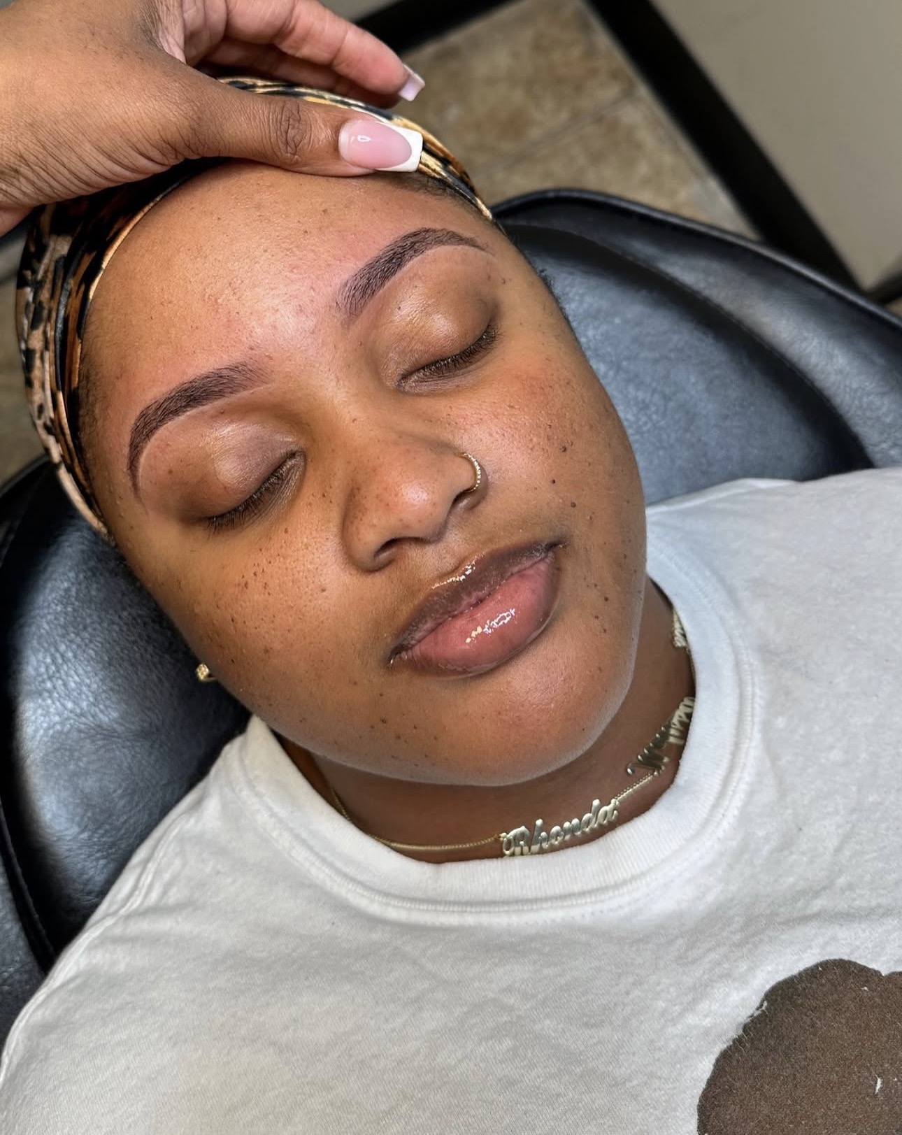 Woman with closed eyes receiving a beauty treatment on her forehead, lying on a chair.