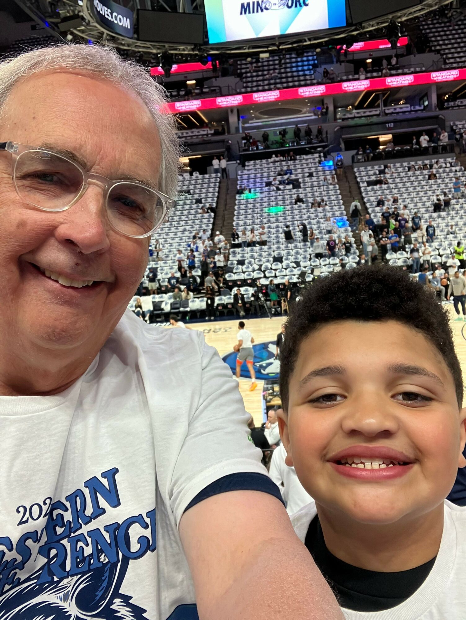 Close-up of an older man and a young boy smiling at a sports arena with empty seats in the background.