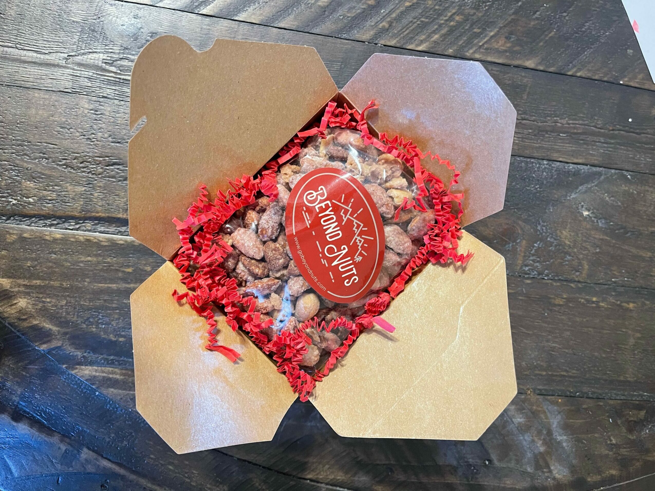 Open cardboard box with red shredded paper and a chocolate treat with a red label inside.