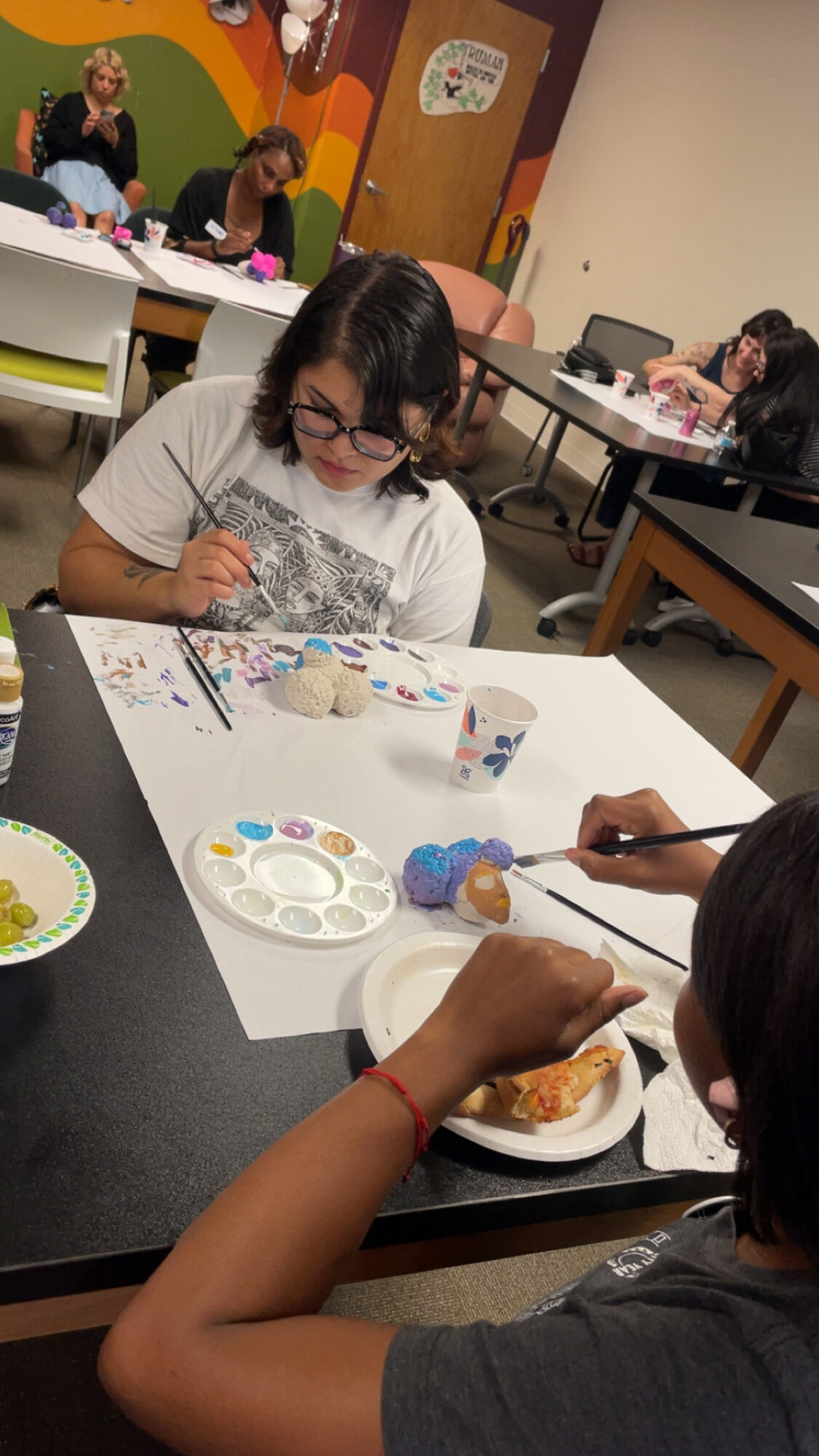 Children painting and eating at a table in a classroom or art space.