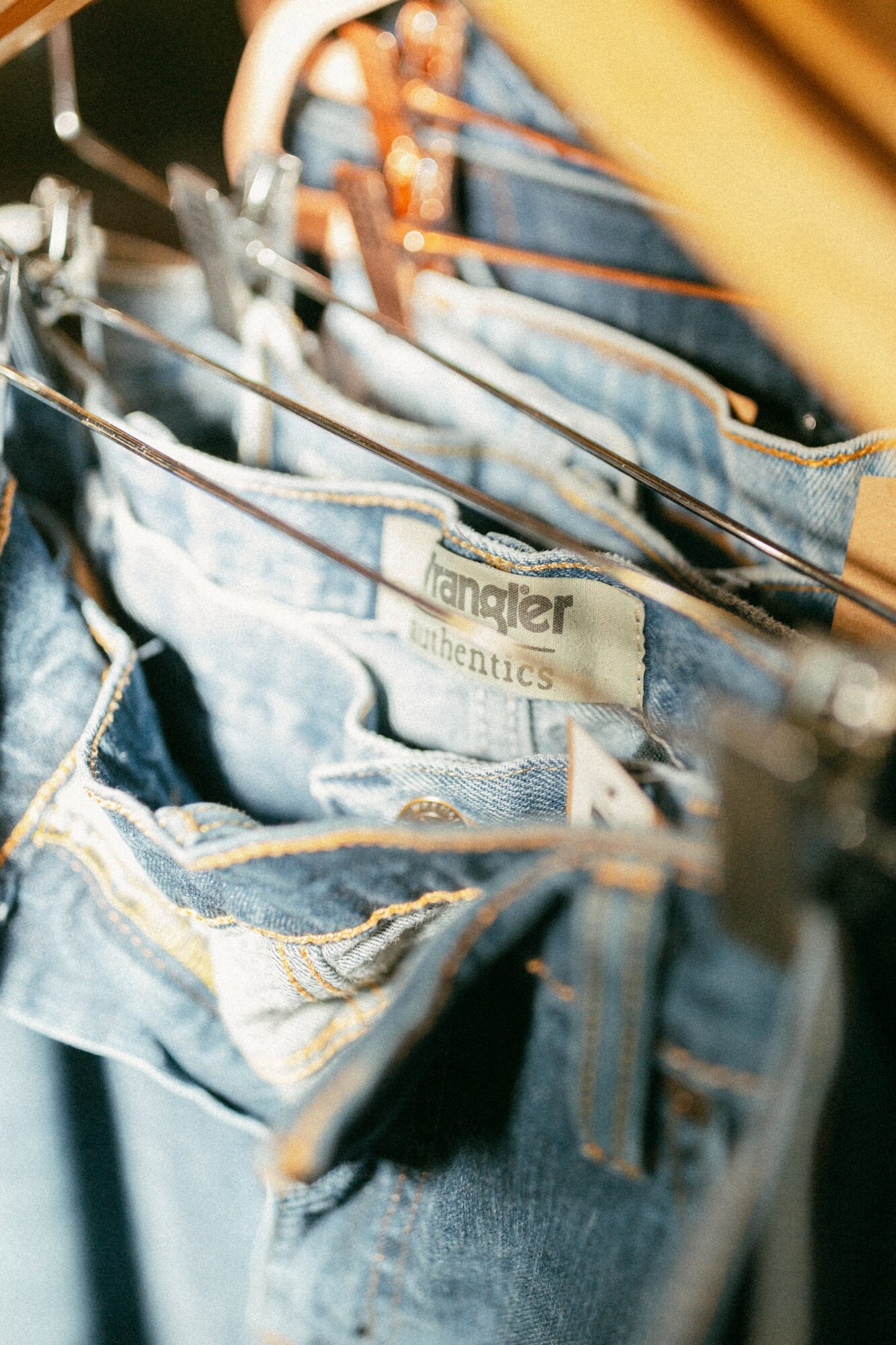 Close-up of denim jeans hanging on a rack with a Wrangler label visible.