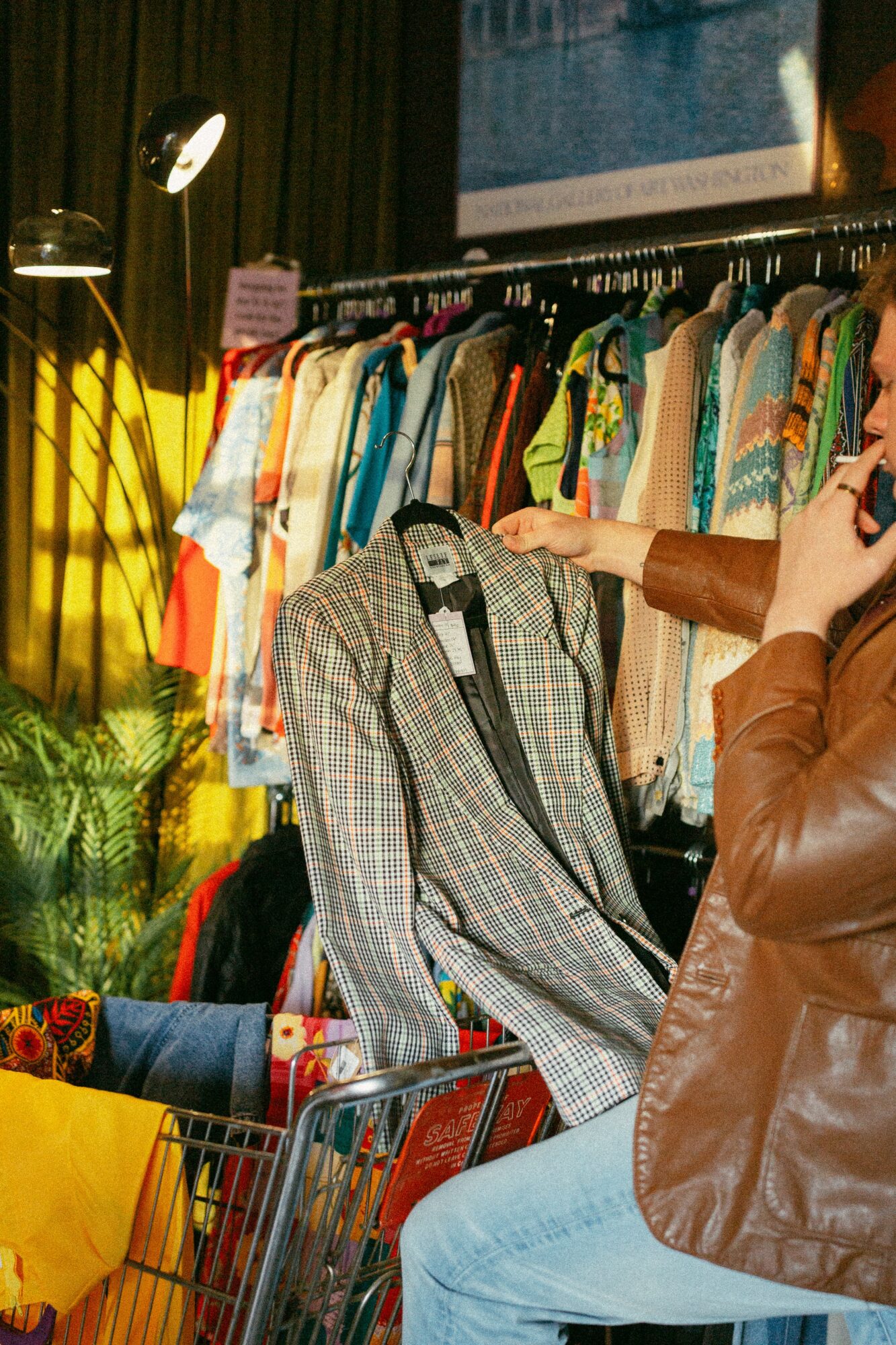 Person shopping for clothes, holding a checkered blazer, in a store with colorful garments on racks.