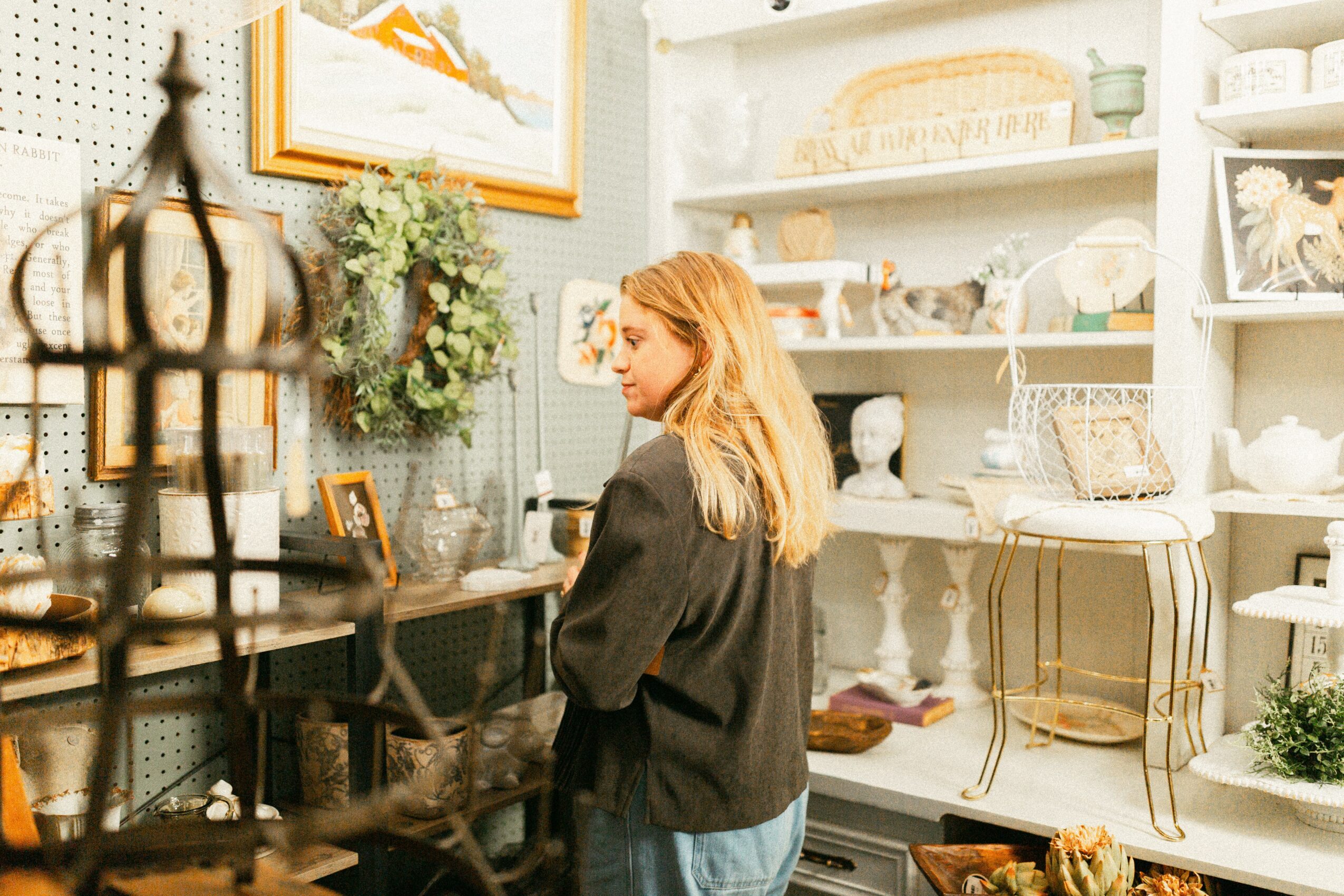 Woman with blonde hair browsing items in a store with shelves of dishes and decorative objects.