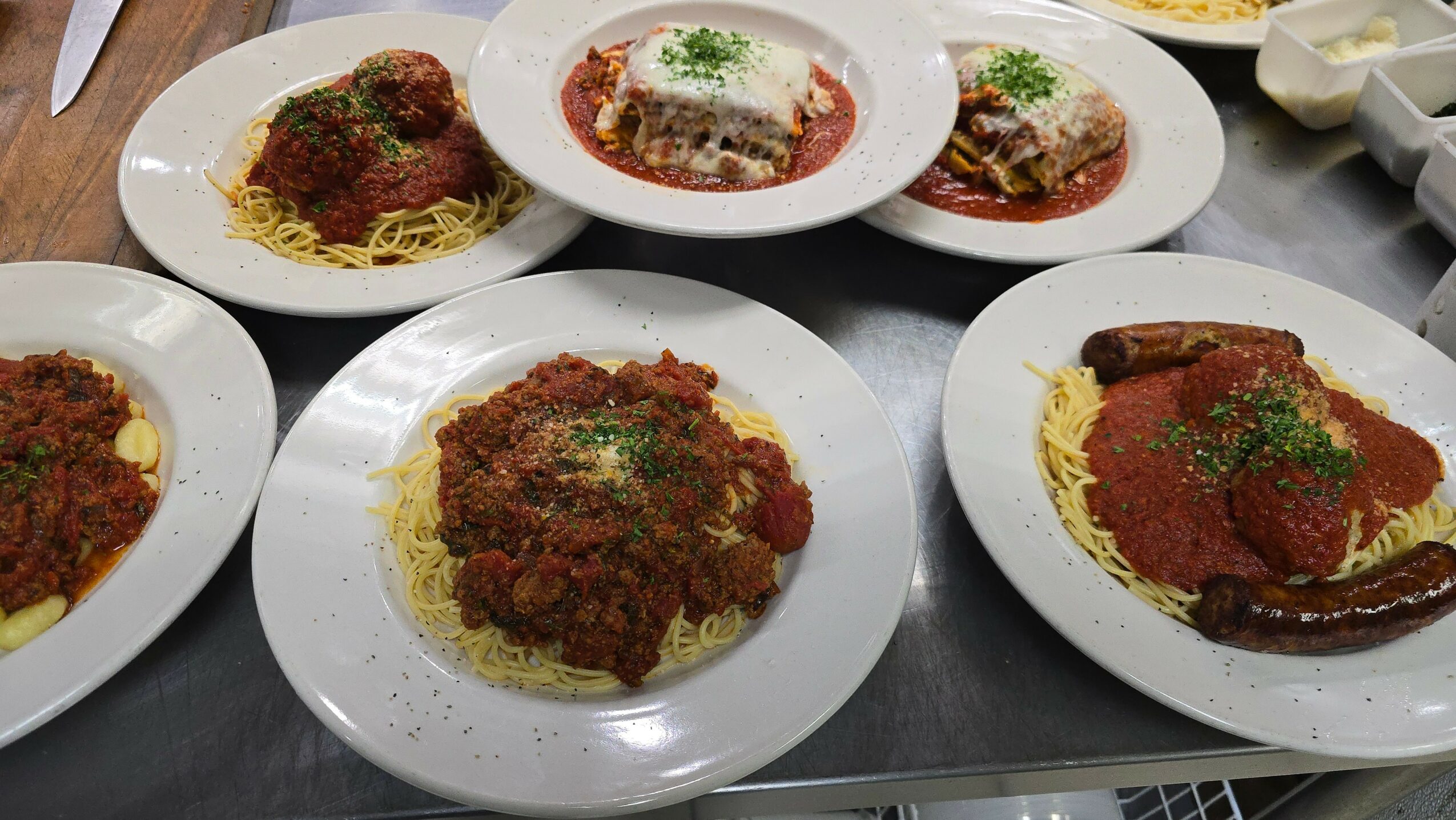 Six plates of spaghetti with meat sauce on a table, some garnished with herbs.