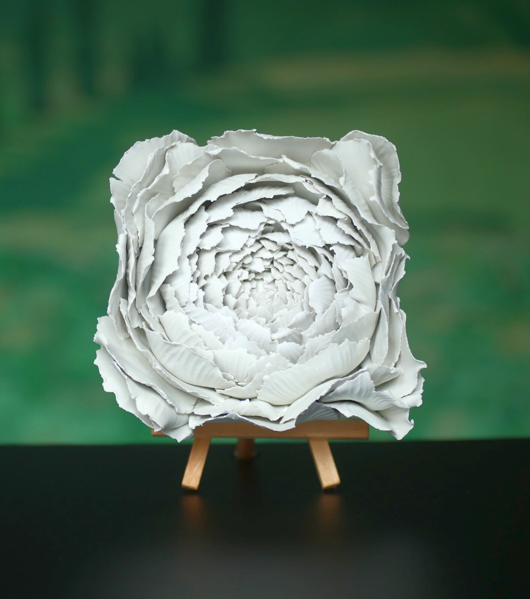 White textured paper sculpture resembling a flower on a small easel against a green background.
