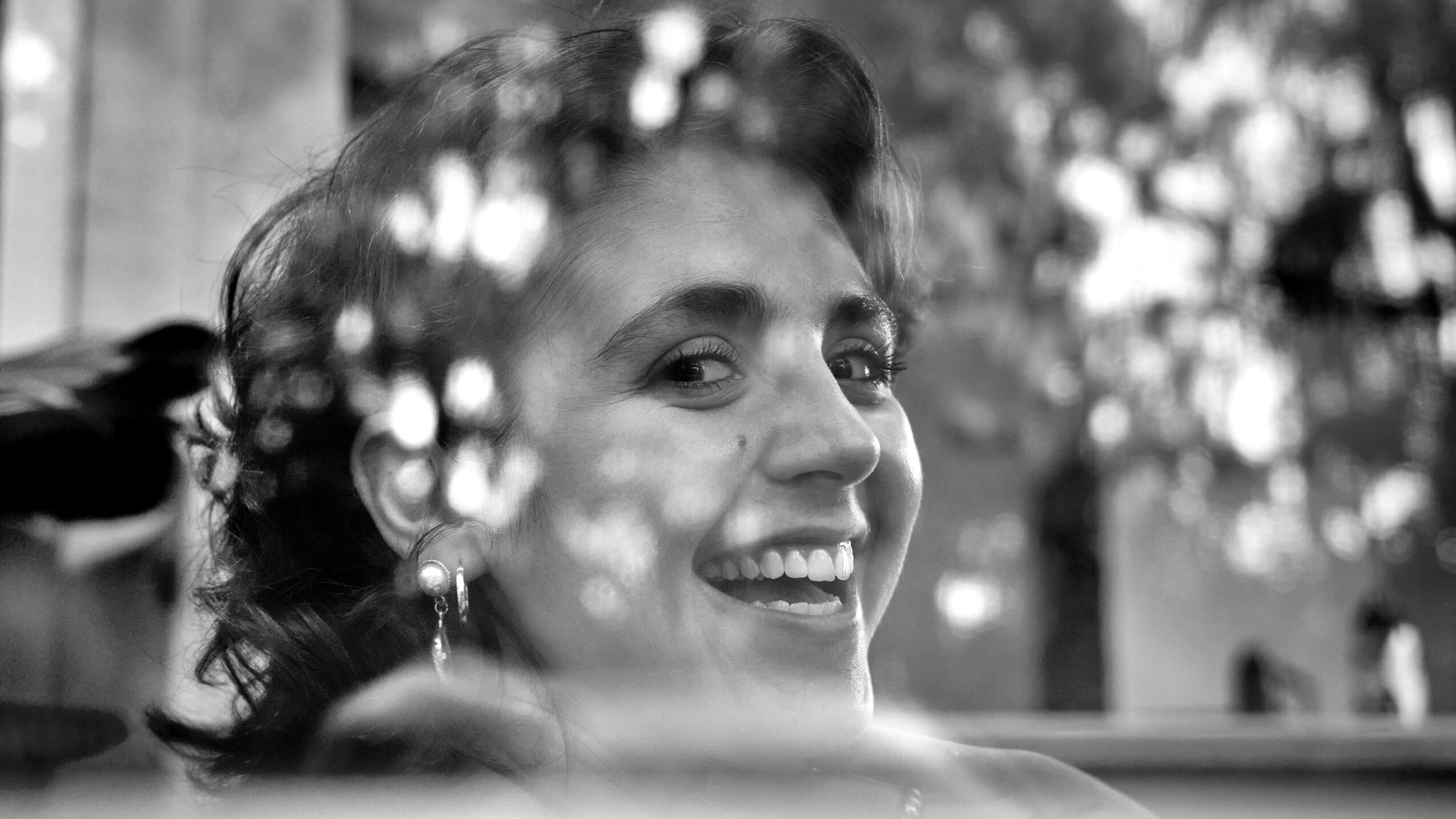 Smiling woman with earrings, reflected in a surface with light spots, outdoors background.