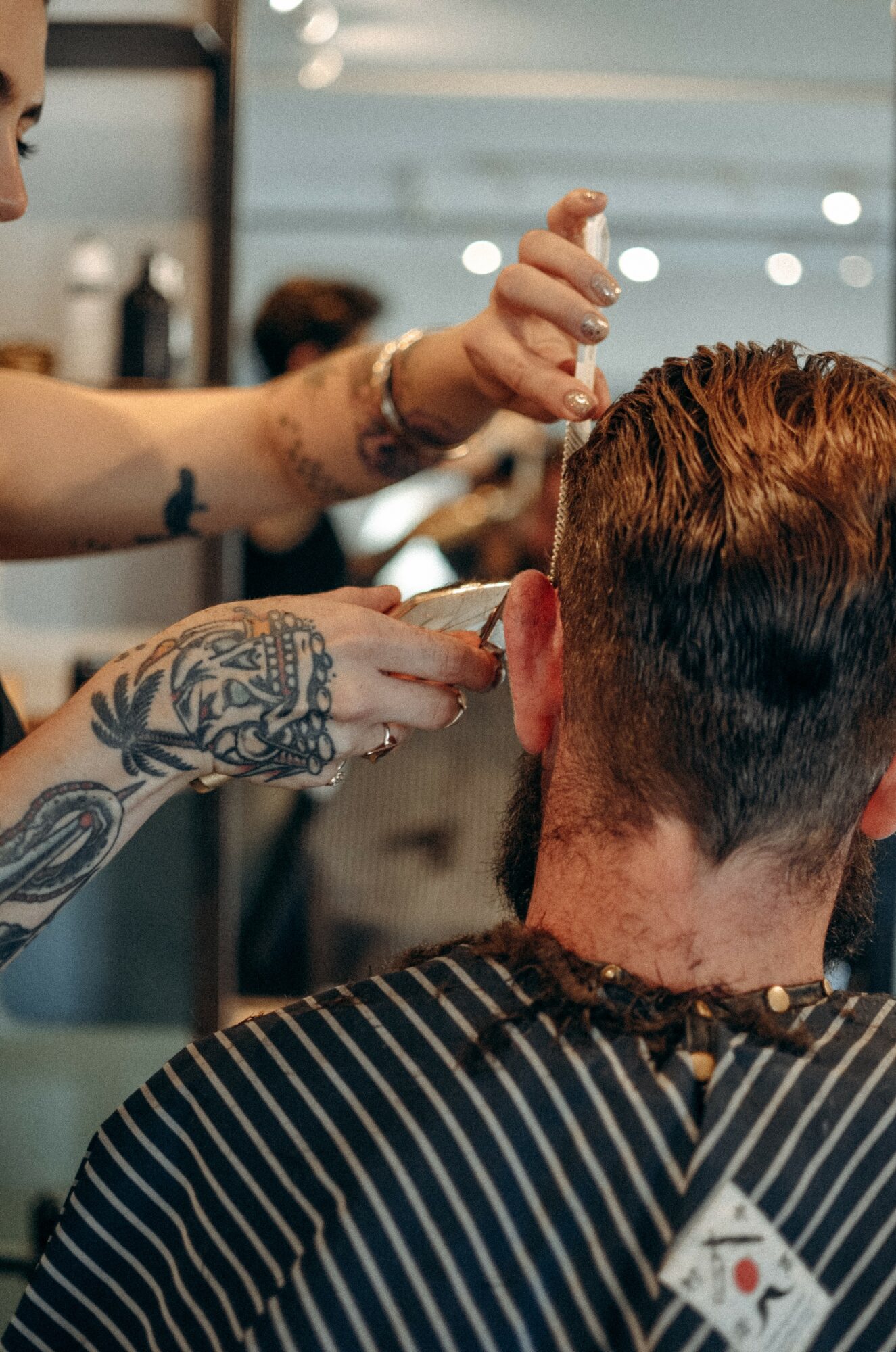 Barber trims a man's hair in a salon, with another stylist visible in the background.