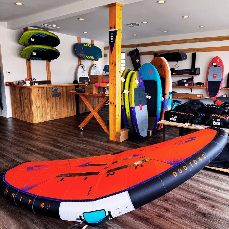 Indoor surf shop with surfboards and paddleboards displayed on walls and floor, wooden counter, and dark wood flooring.
