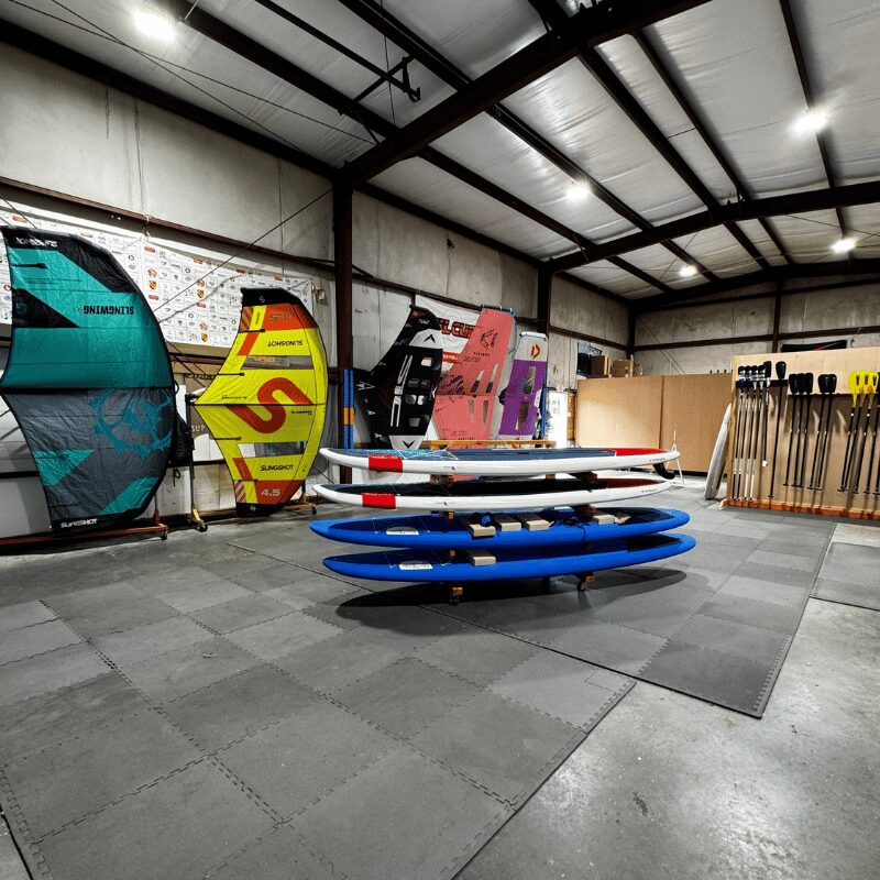 Indoor sports shop with windsurfing boards and paddles displayed on walls and floor.