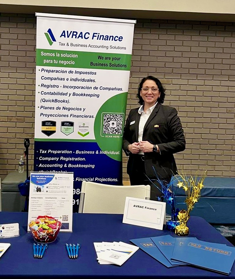 Woman standing next to a banner for AVRAC Finance, smiling, in a conference room with a table and flowers.