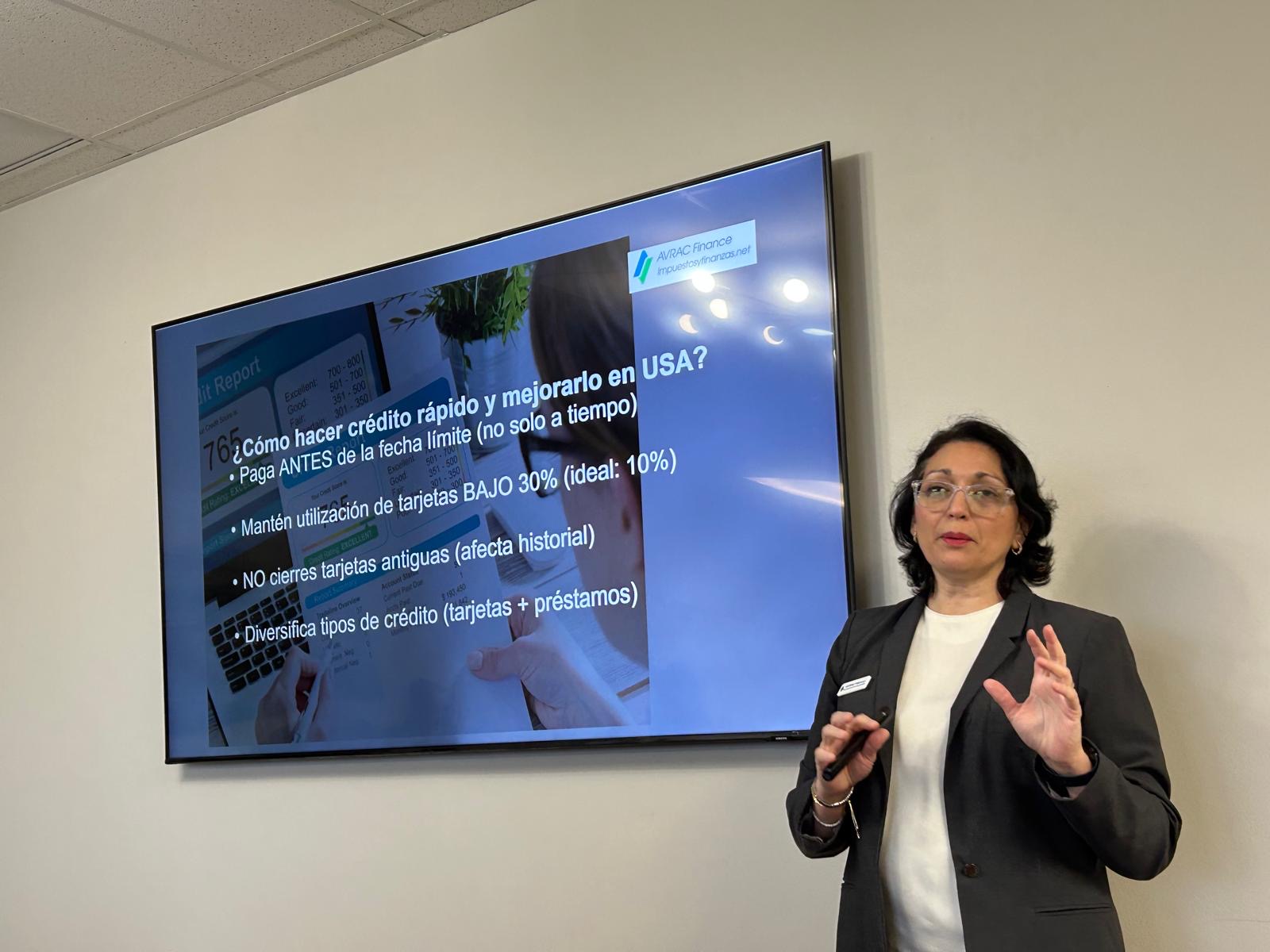 Woman in glasses and blazer giving a presentation in front of a large screen displaying text and images.