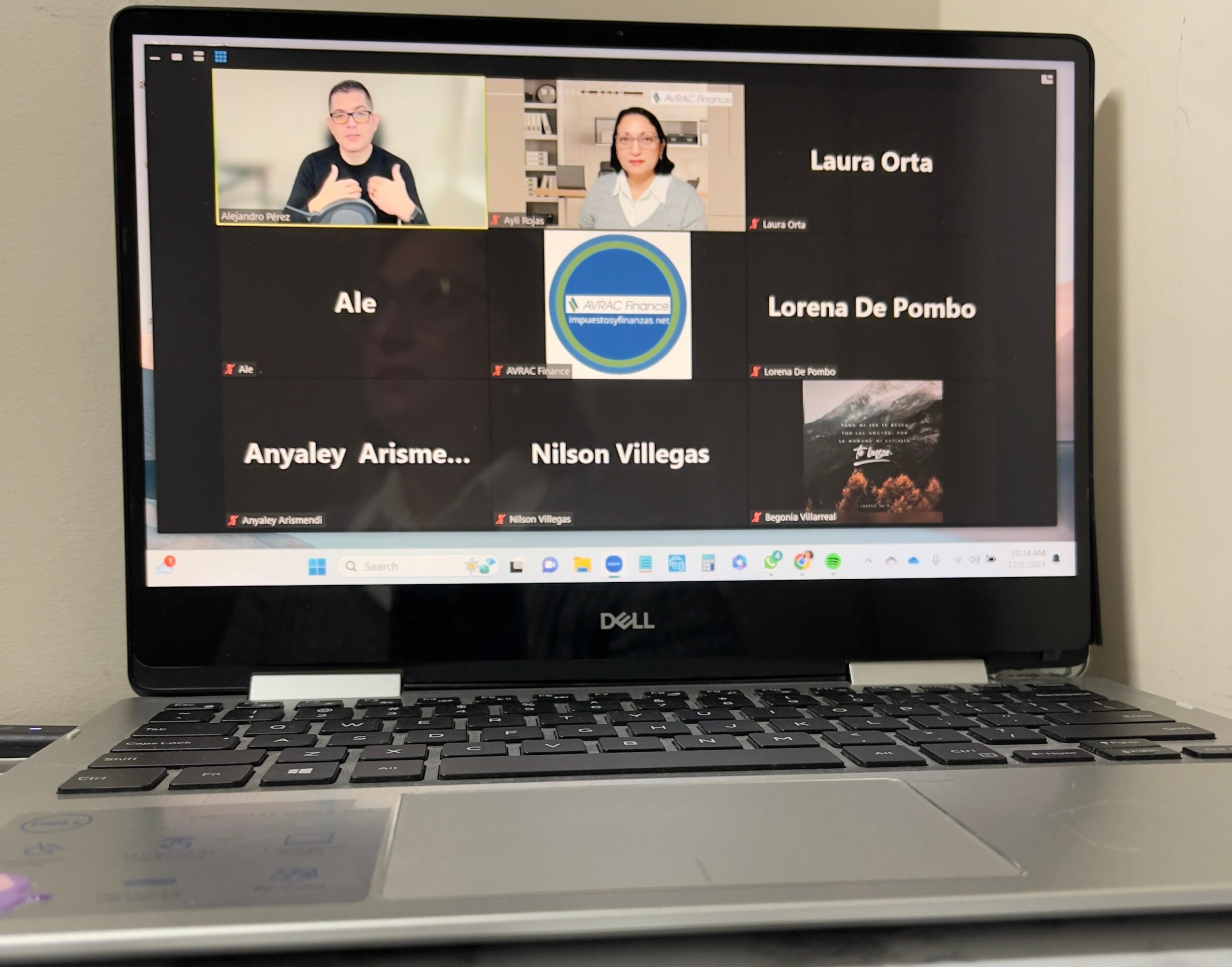 Laptop screen displaying a video conference with six participants, some with visible names, in a grid layout.