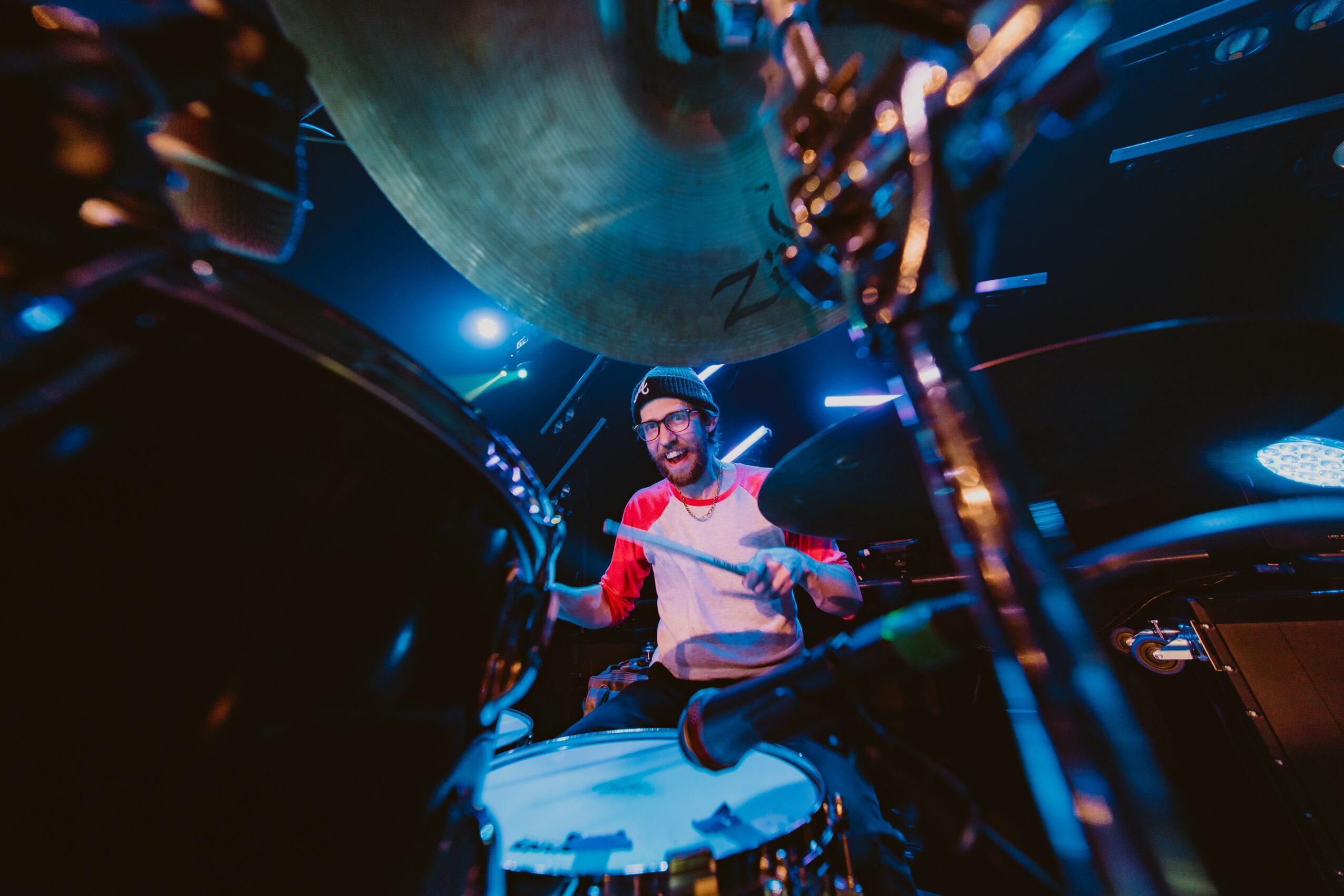 A DJ wearing headphones and a red and white shirt performs with turntables in a dark, colorful setting.