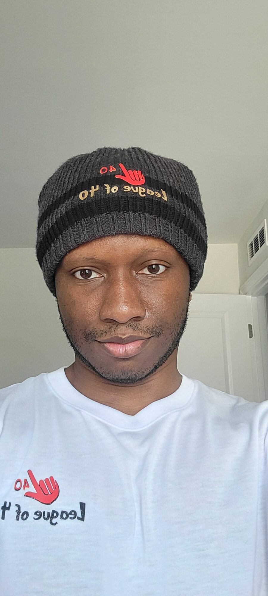 Young man wearing a black beanie and white T-shirt, looking at the camera, standing indoors.