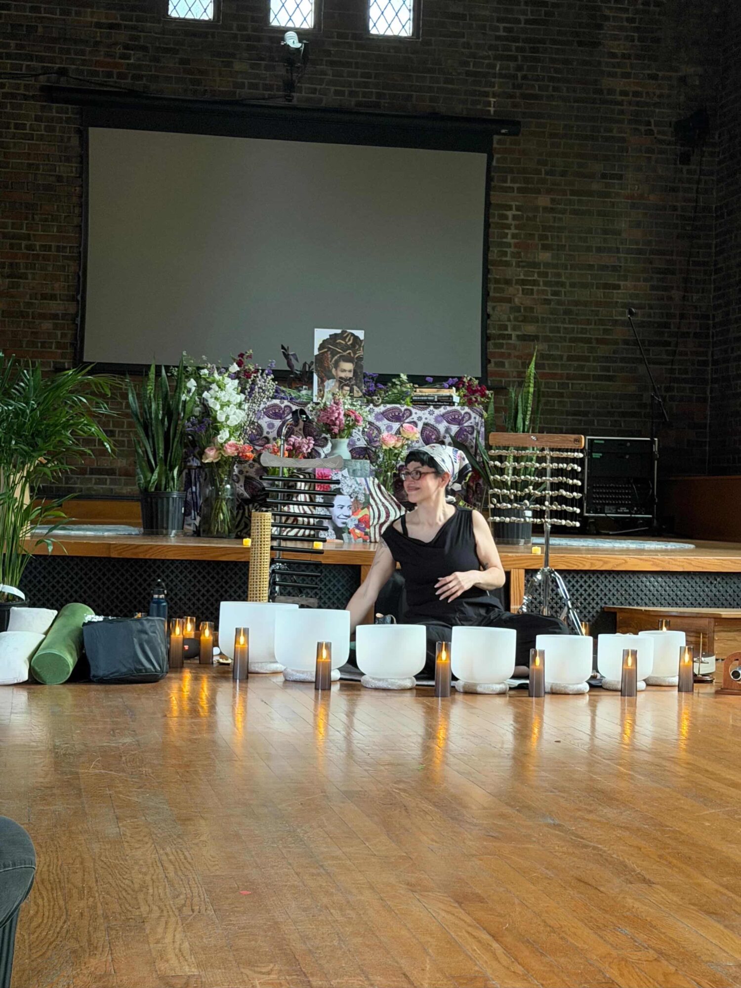 Child sitting at a table with cups, in a room with a large screen and floral decorations, brick wall background.