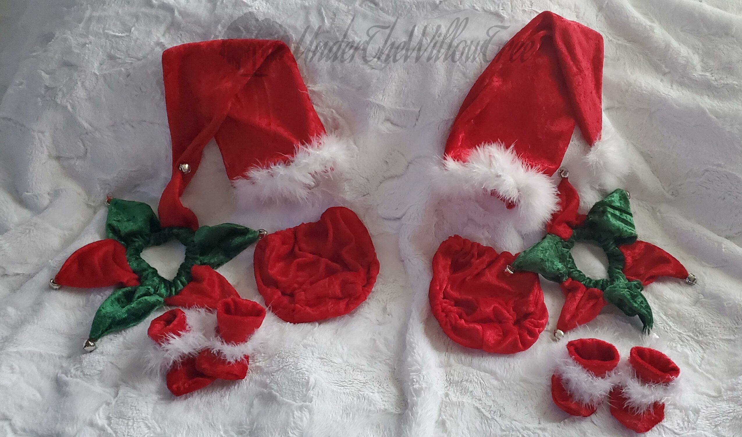 Two red Santa hats with white trim, green holly leaves, red berries, and small red and white mittens on a white fabric background.