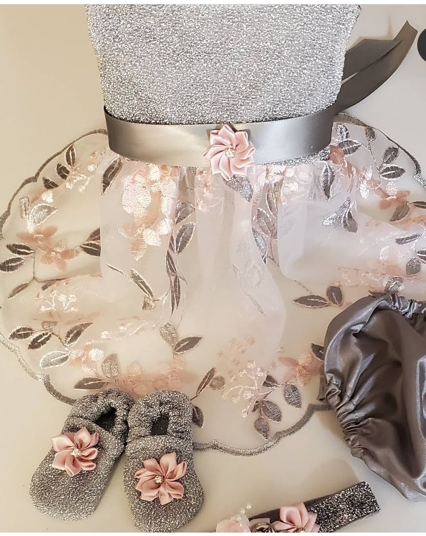 Child's dress with floral tulle skirt, gray shoes with pink flowers, and a gray satin bag, all arranged on a surface.