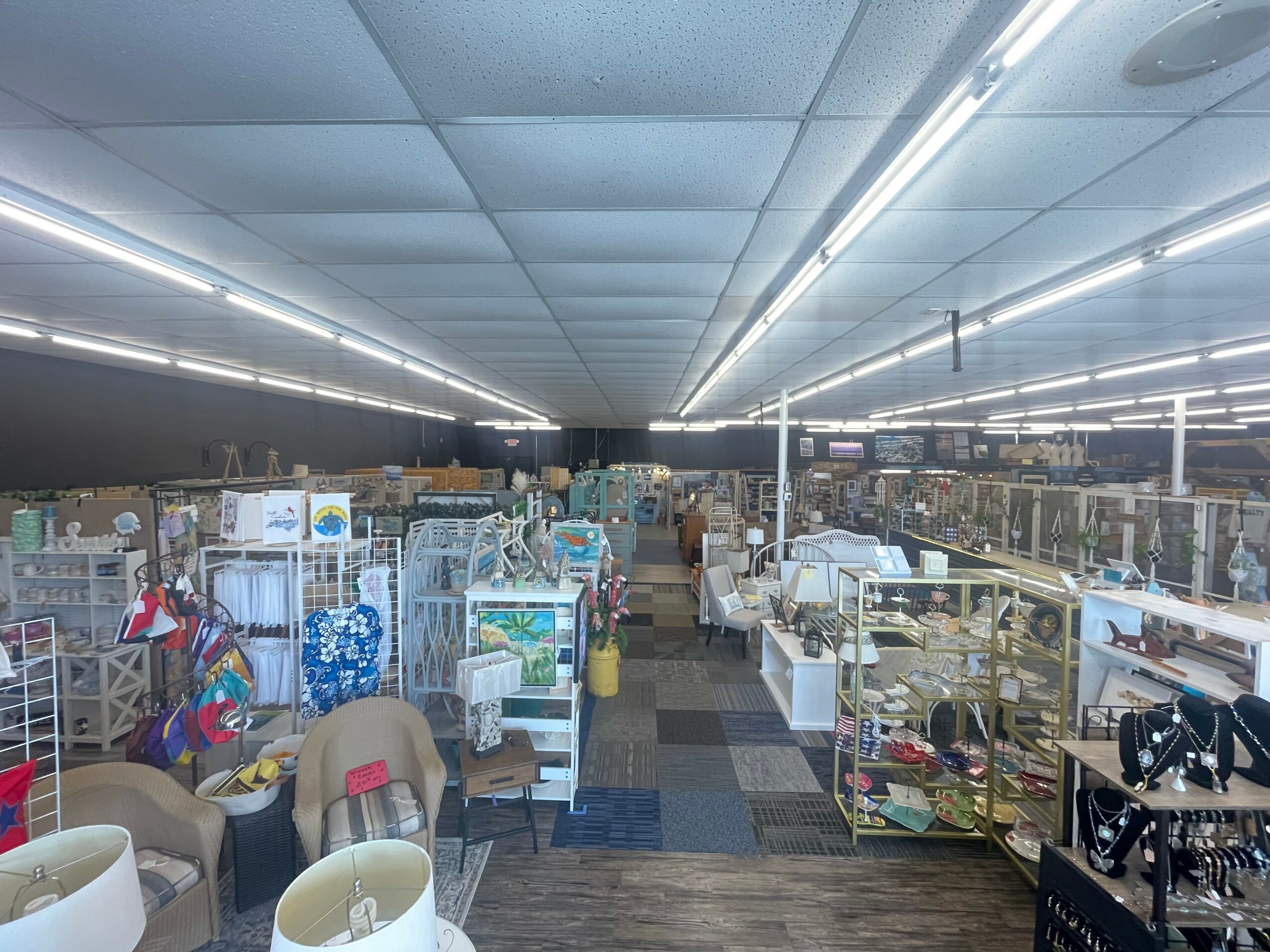 View of a large store with shelves and displays filled with various products, ceiling with fluorescent lights, and a central aisle.