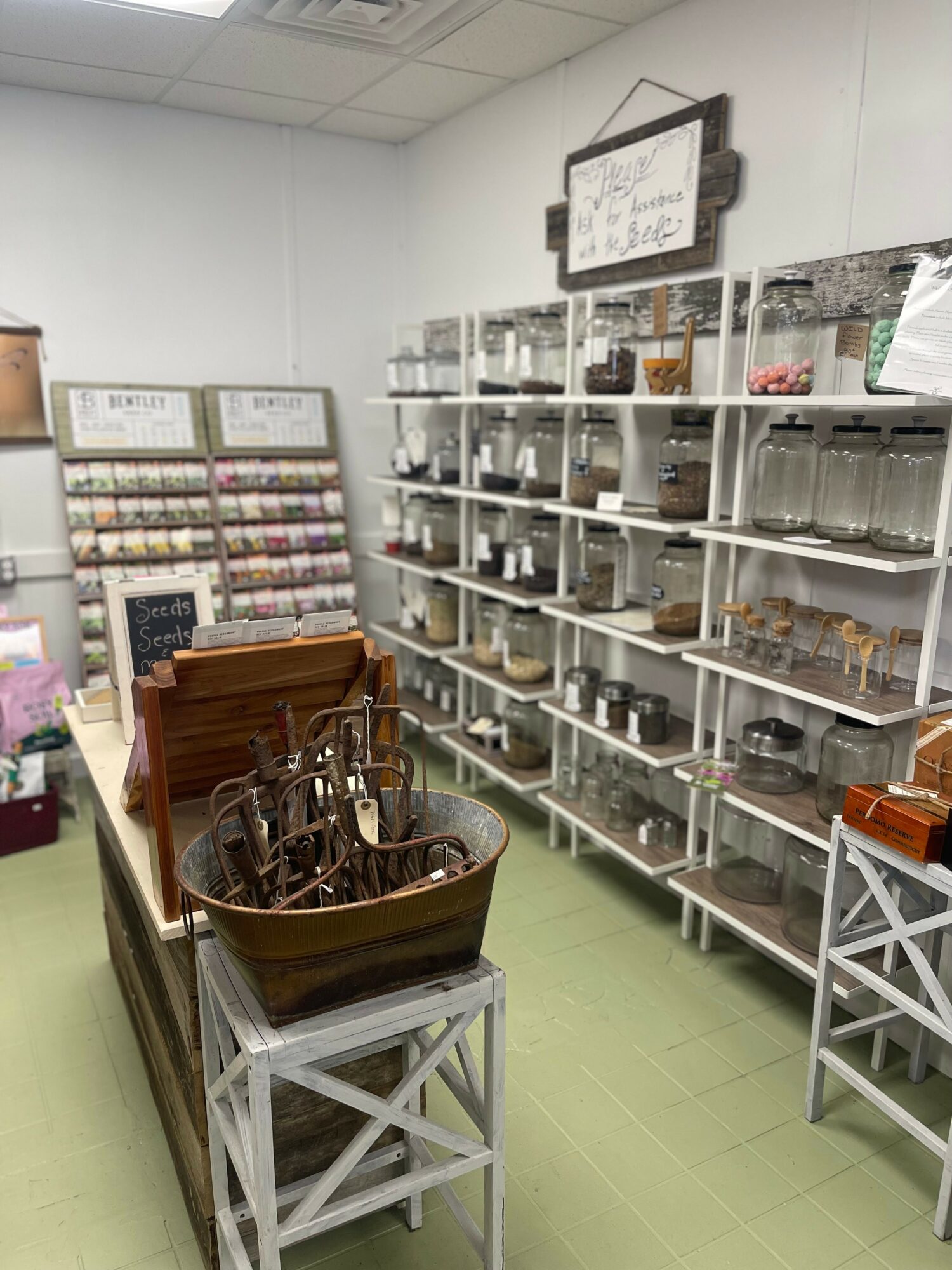 Store interior with shelves of small items, a basket on a stand, and display racks, with a light-colored floor.