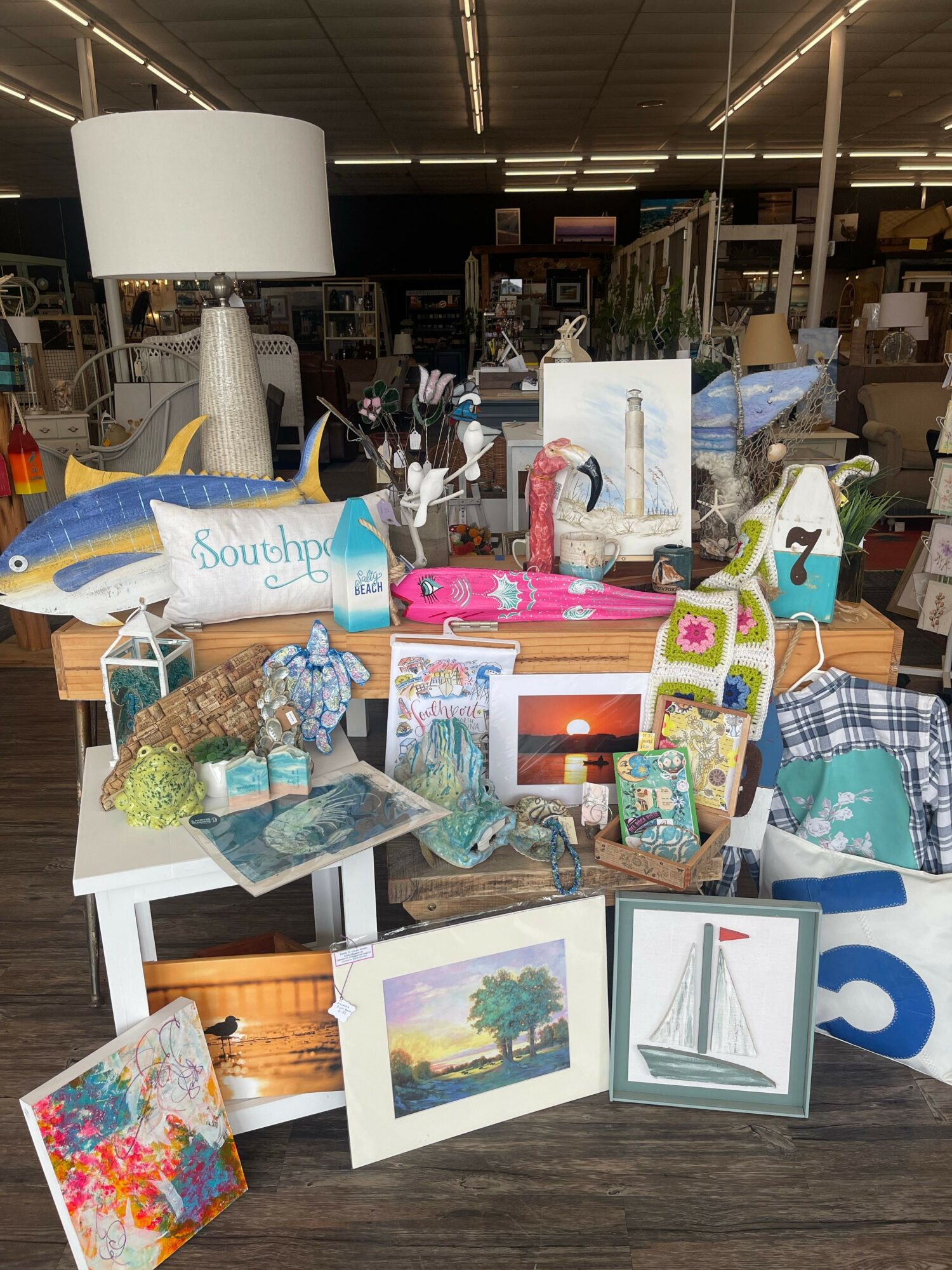 Table with various colorful items, framed pictures, and decorative objects in a store setting.