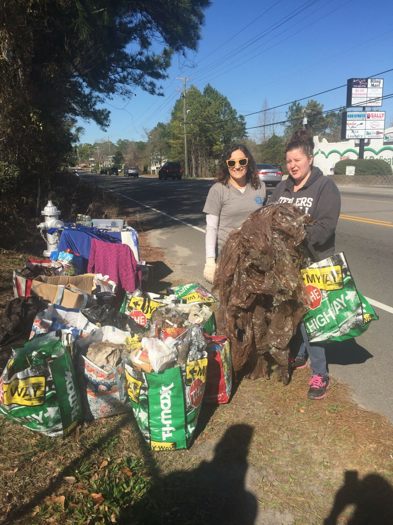Three people standing outdoors near a table with bags of snacks and supplies, with trees and power lines in the background.