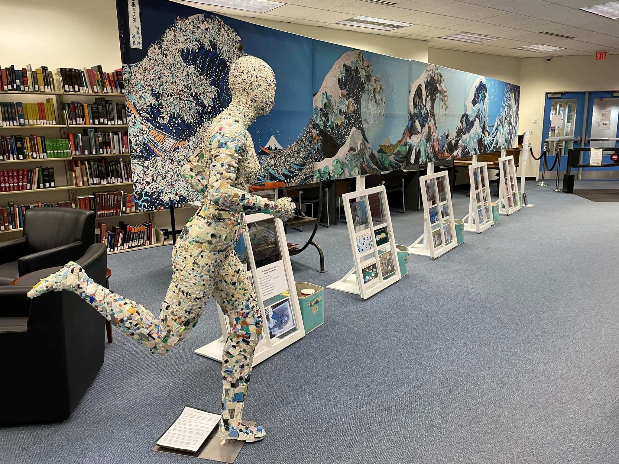 A sculpture of a running person made of small objects, with a mural of mountains and trees in the background.