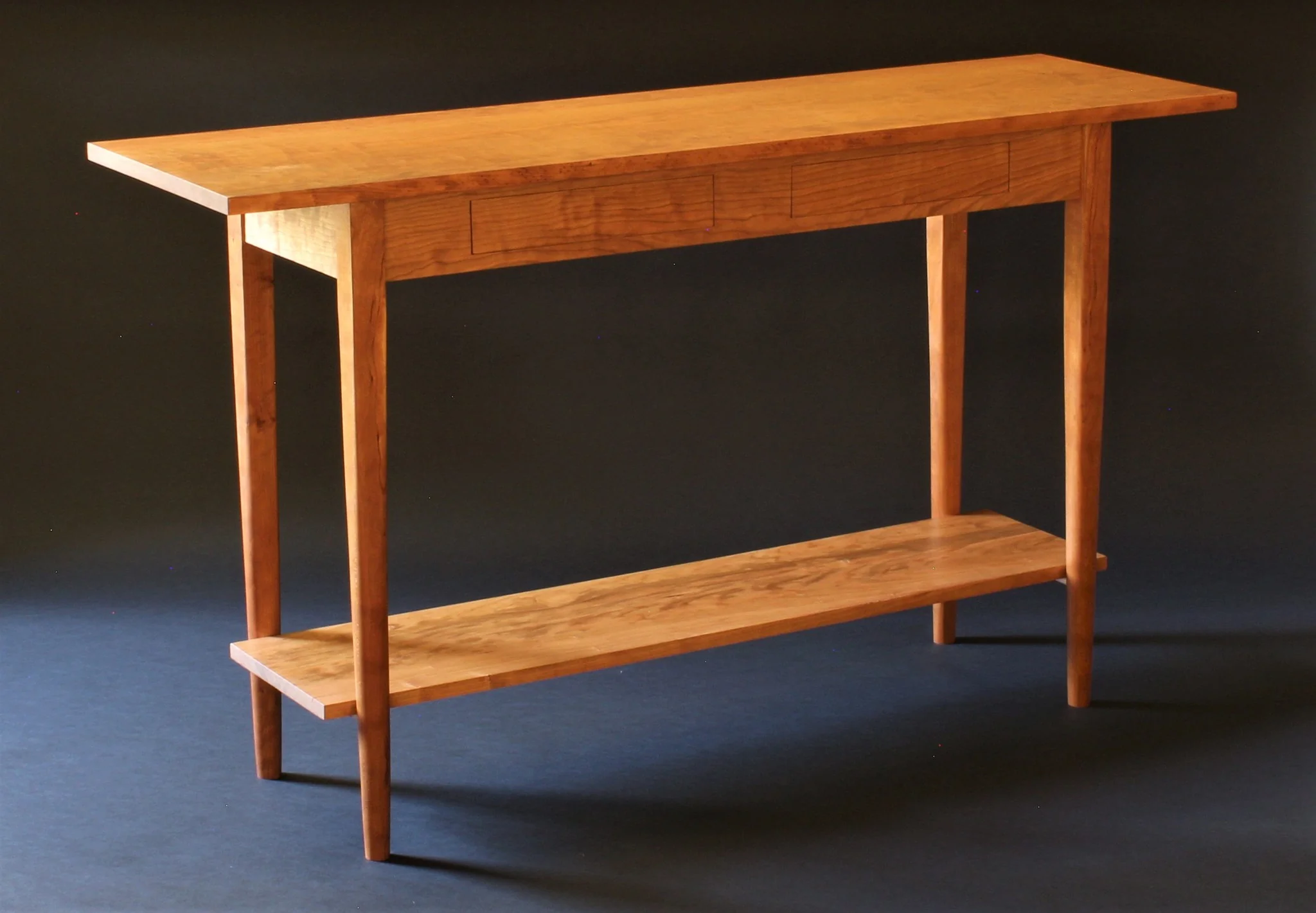 Wooden table with a lower shelf, four legs, and a flat rectangular top, set against a dark background.