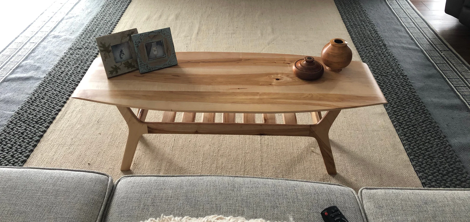 Wooden coffee table with decorative items on top, placed on a beige and dark border rug in a living room.