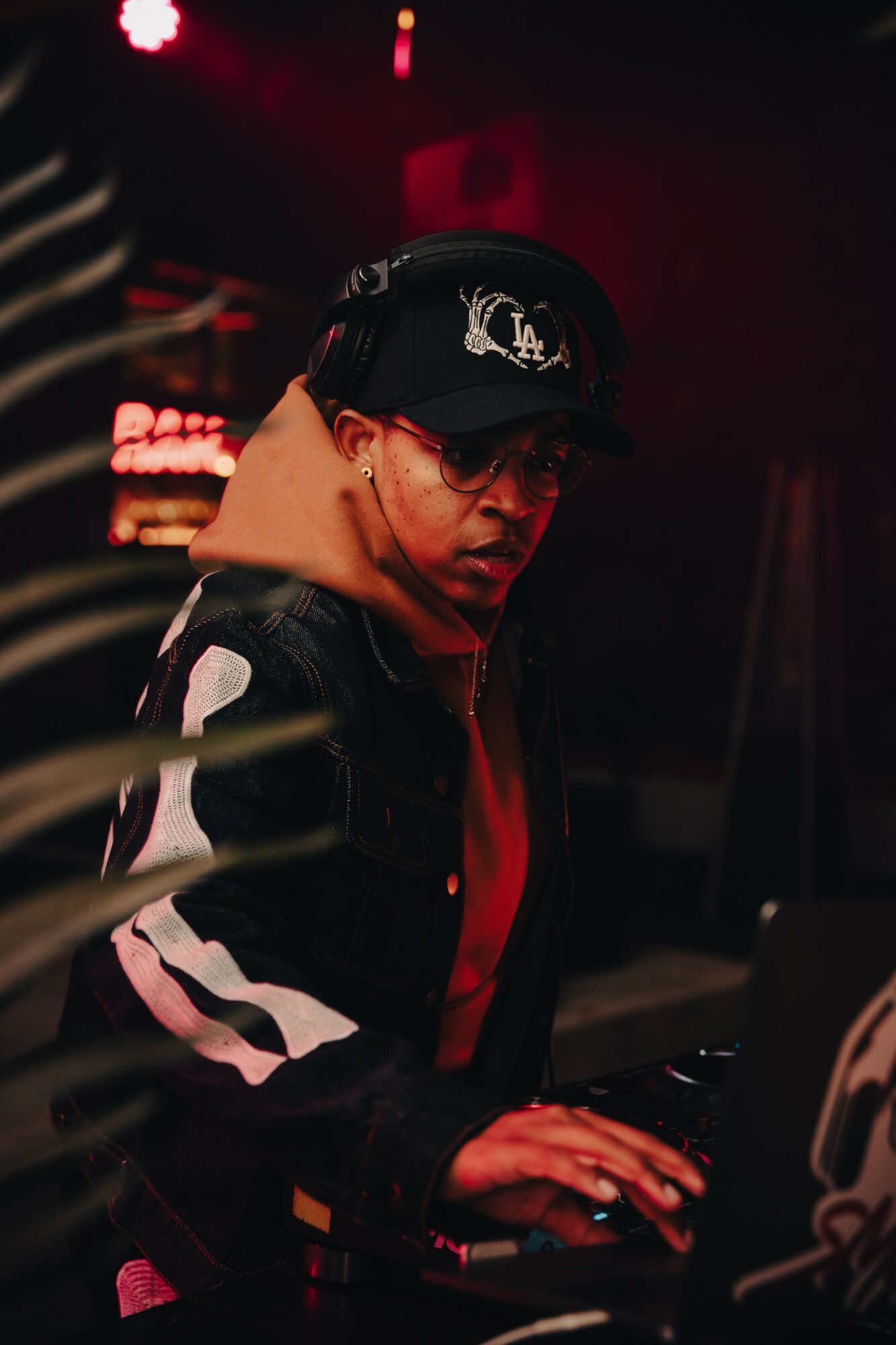 Person wearing a cap and glasses, focused on a computer in a dimly lit environment.