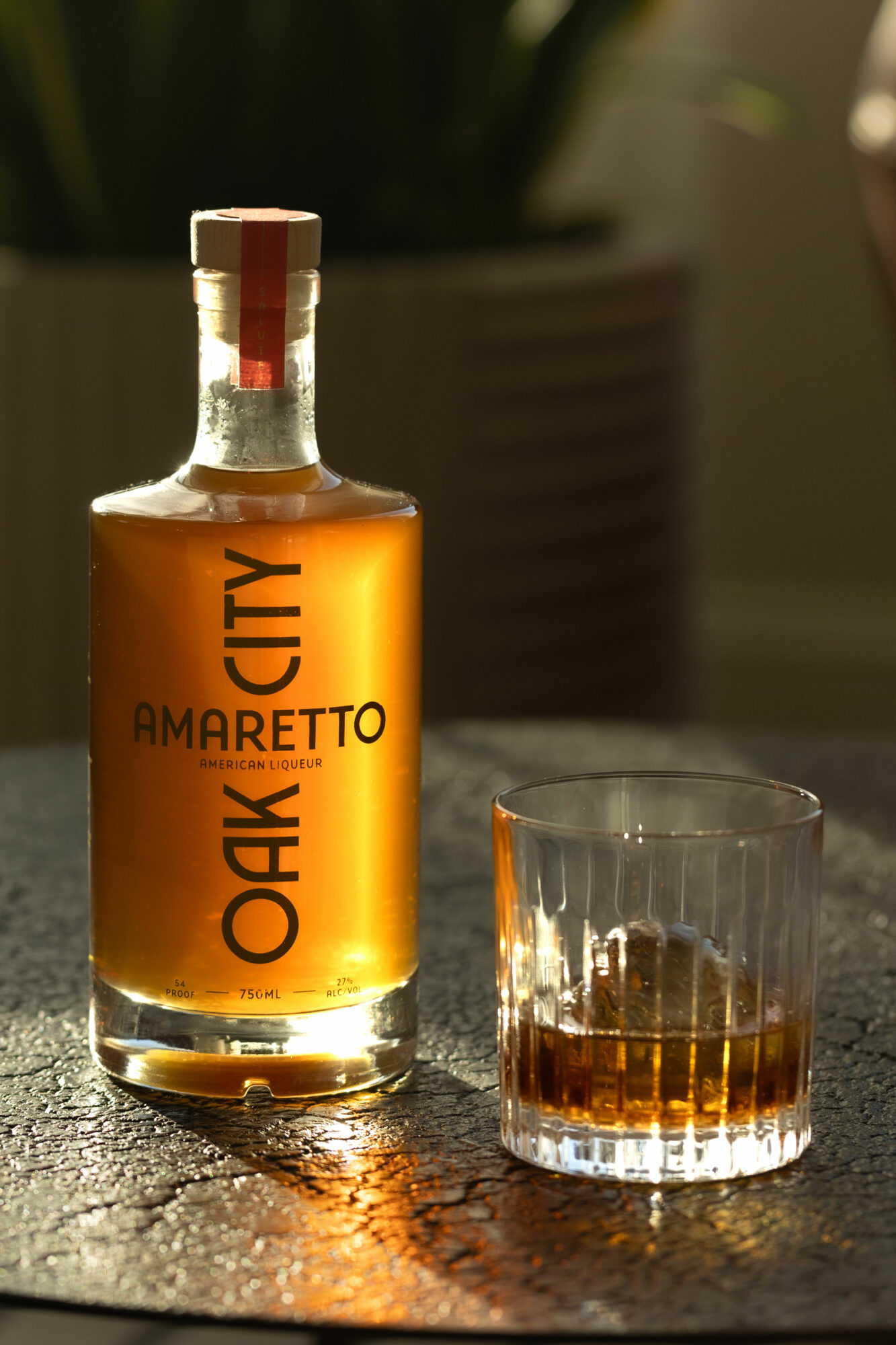 Bottle of Amaretto liqueur and a glass with some liquid on a textured surface, background blurred.
