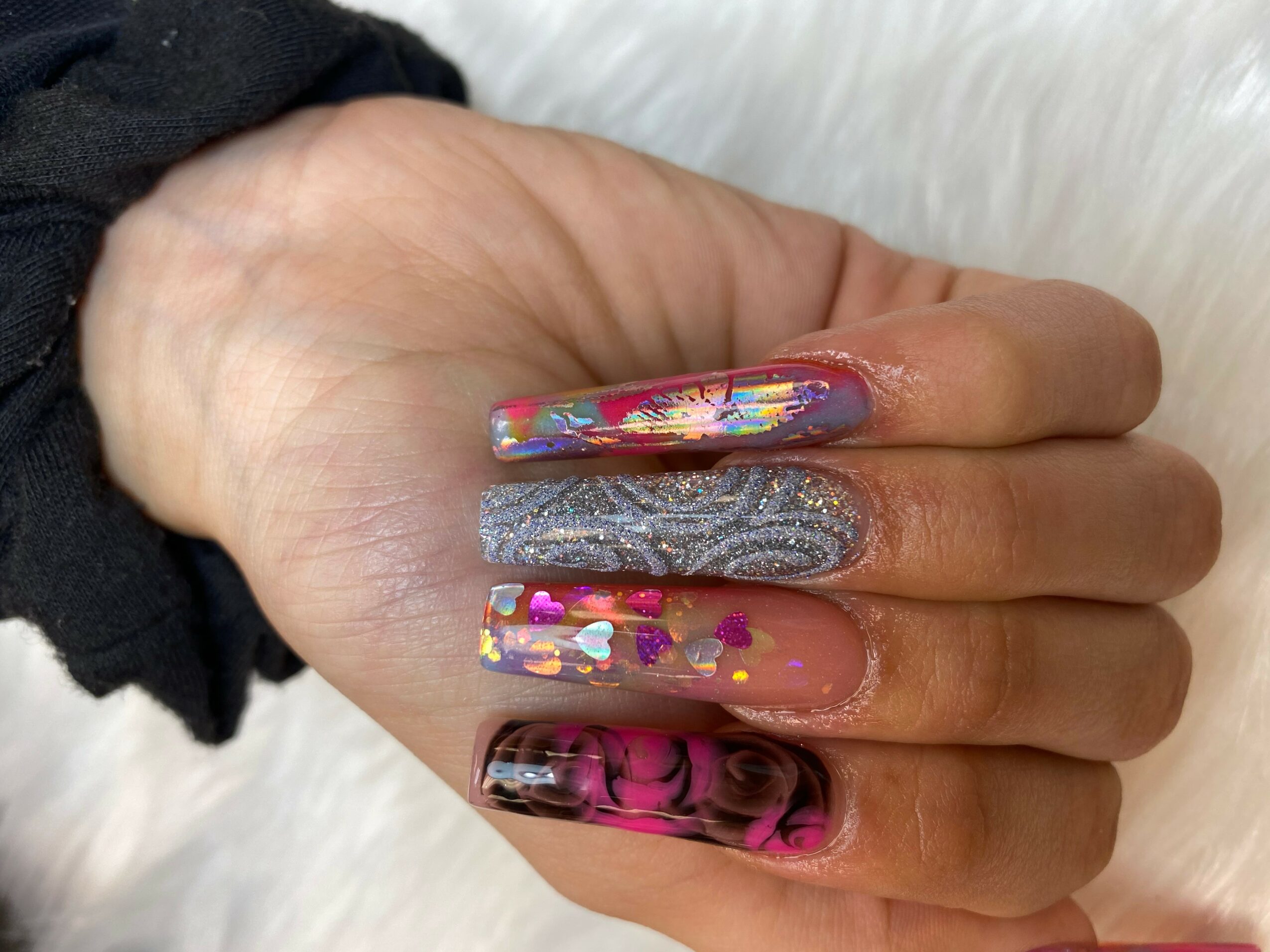 Hand with colorful, decorated nails resting on a white surface, with a black sleeve partially visible.