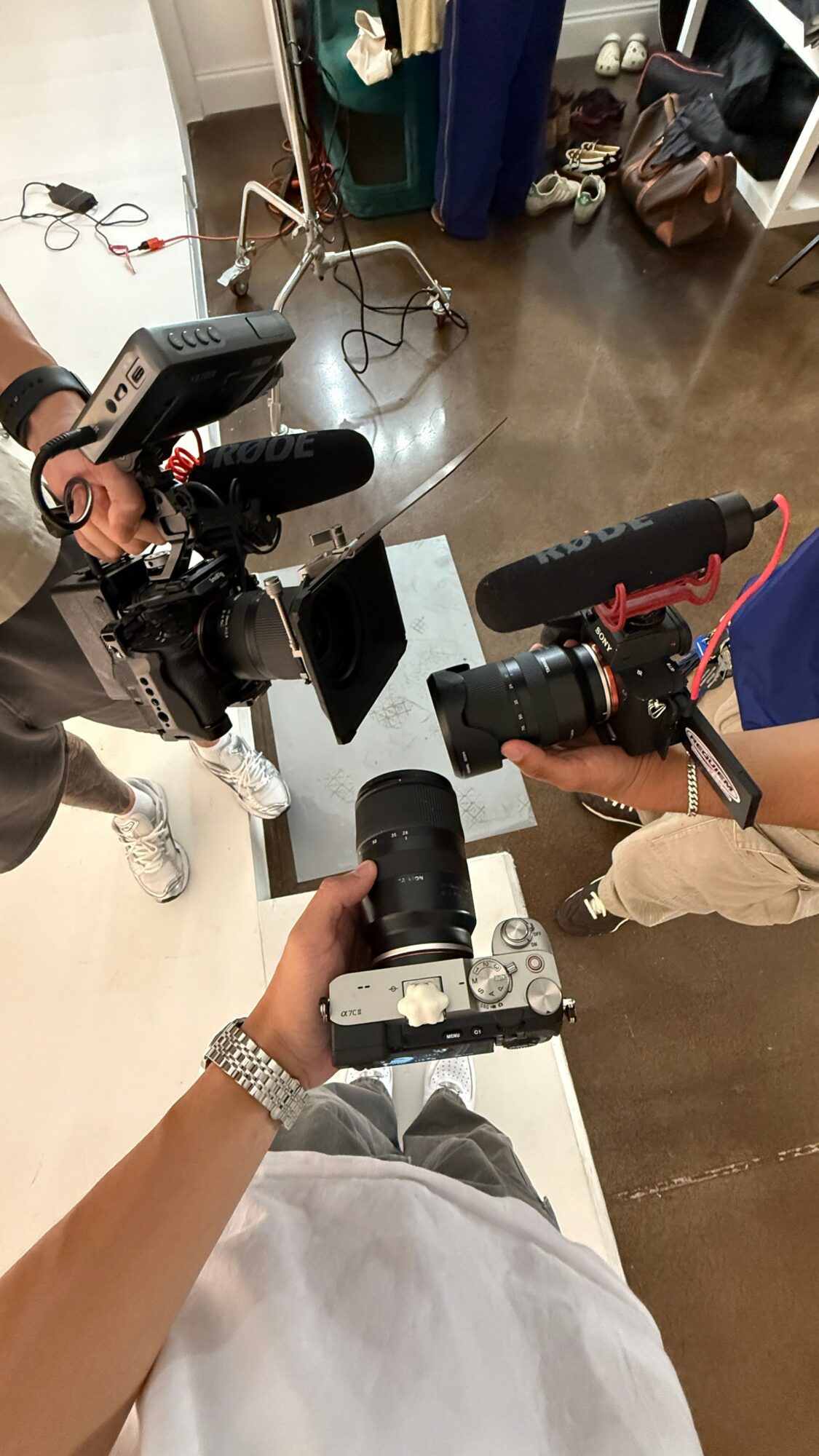 Three people holding cameras over a white table in a room with a wooden floor and shelves.
