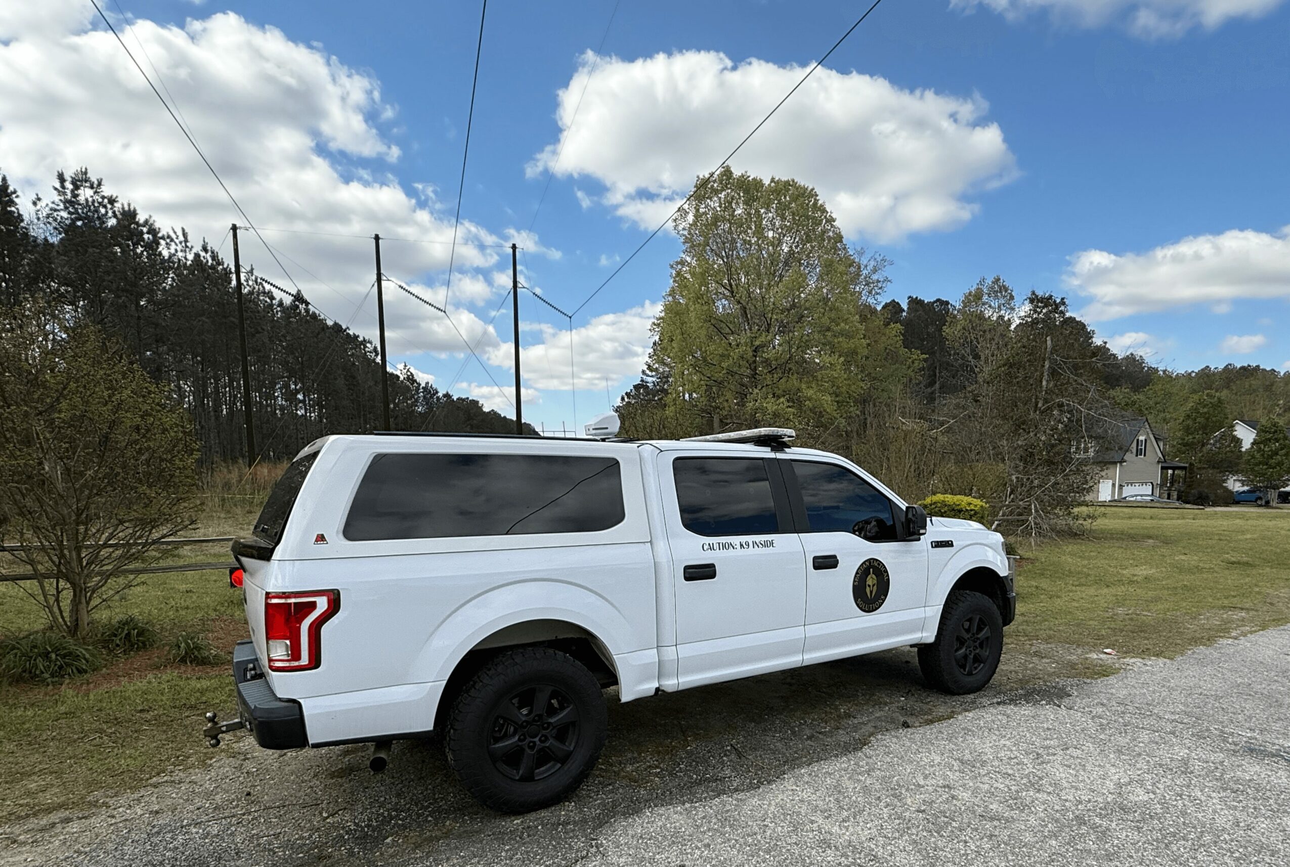 White vehicle parked on gravel with trees and blue sky in background.