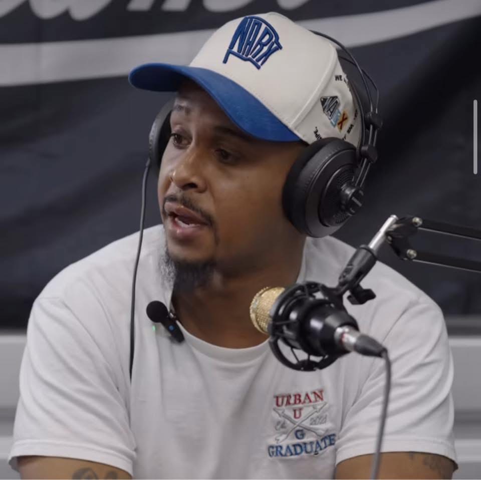 Man wearing a white cap and headphones speaking into a microphone during a broadcast.