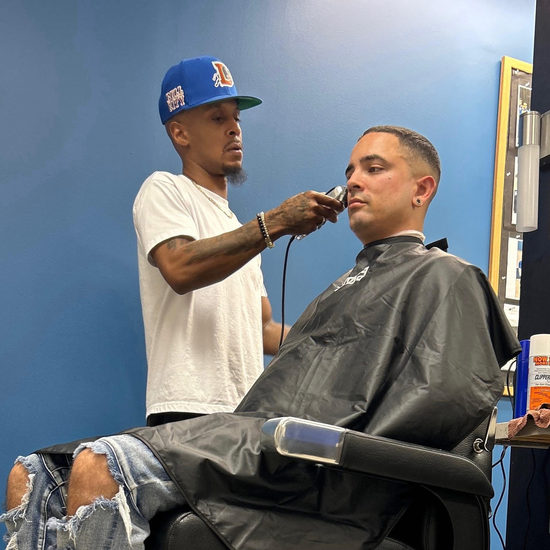 Barber giving a haircut to a man in a barber shop, with a blue wall background.