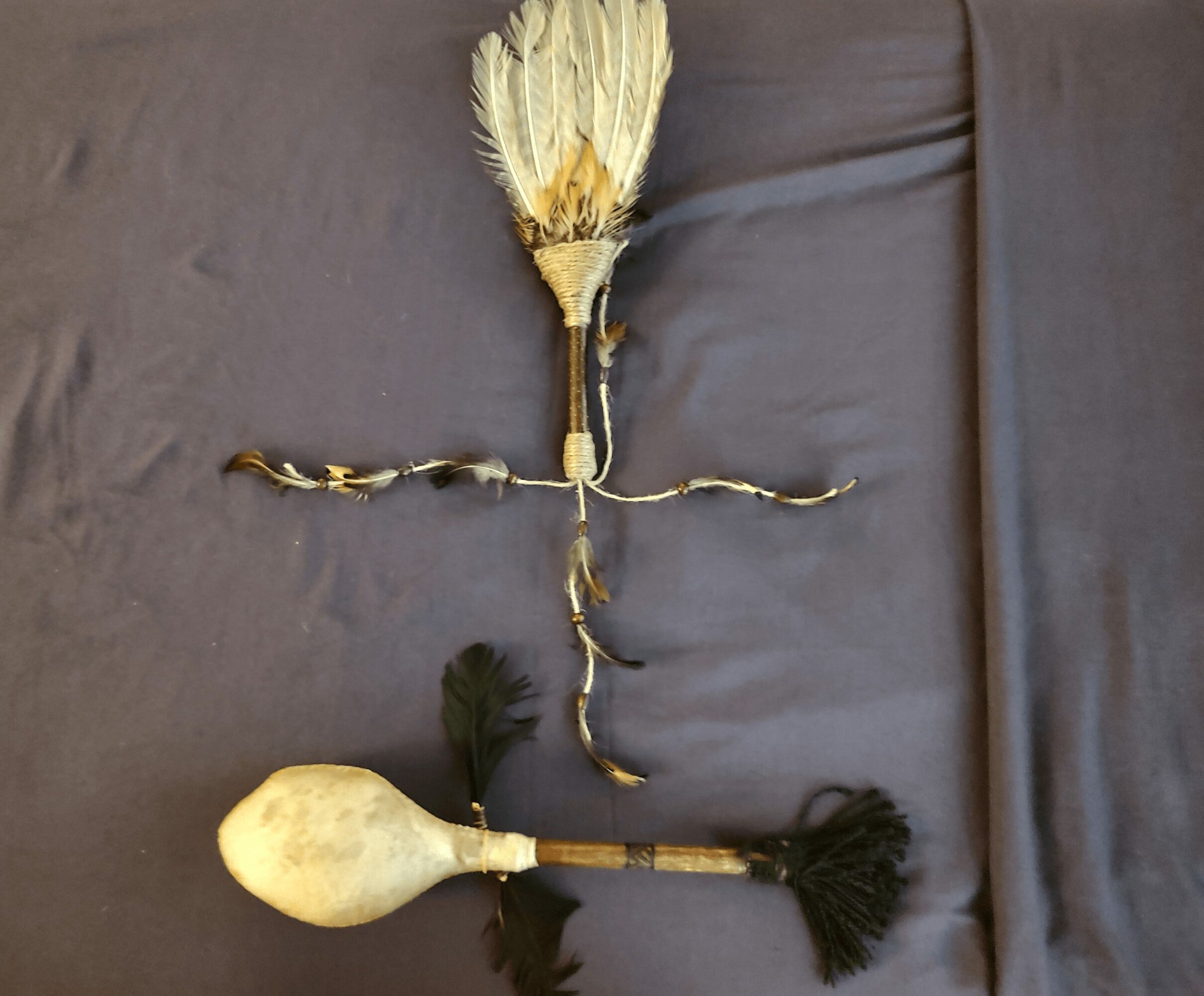 A broom, a small plant, and a gourd with a tassel are arranged on a dark surface.