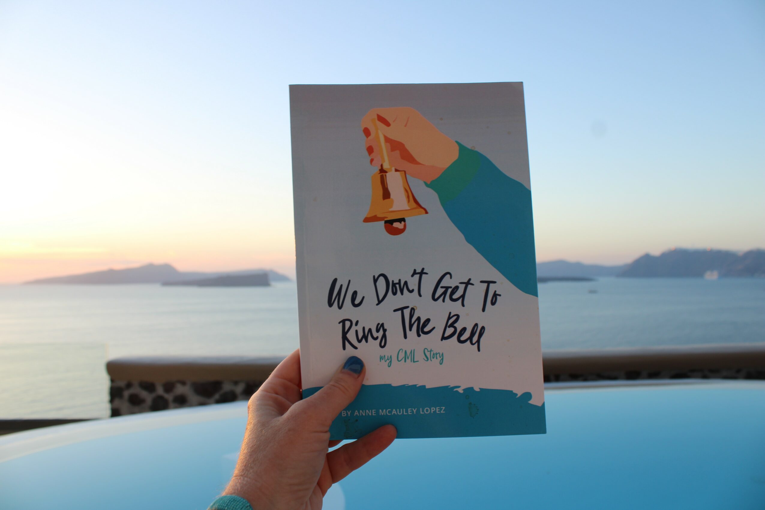 Hand holding a card with a bell and text, against a body of water and sky background.