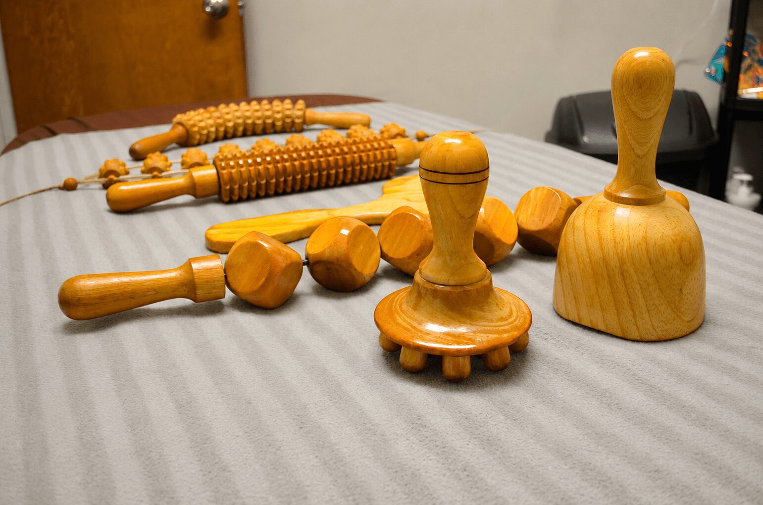 Various wooden massage tools and rollers on a table, with a door and chair in the background.